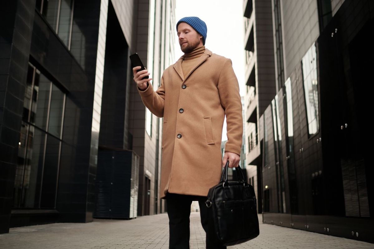 Stylish businessman in a brown coat using smartphone.