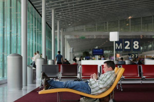 Traveler reclining in an airport lounge while looking at his phone.