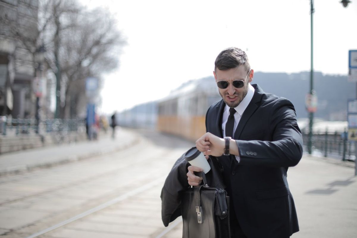 Man in suit with briefcase and coffee checking time.