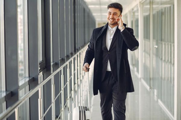 Business traveler in corridor with suitcase and phone.