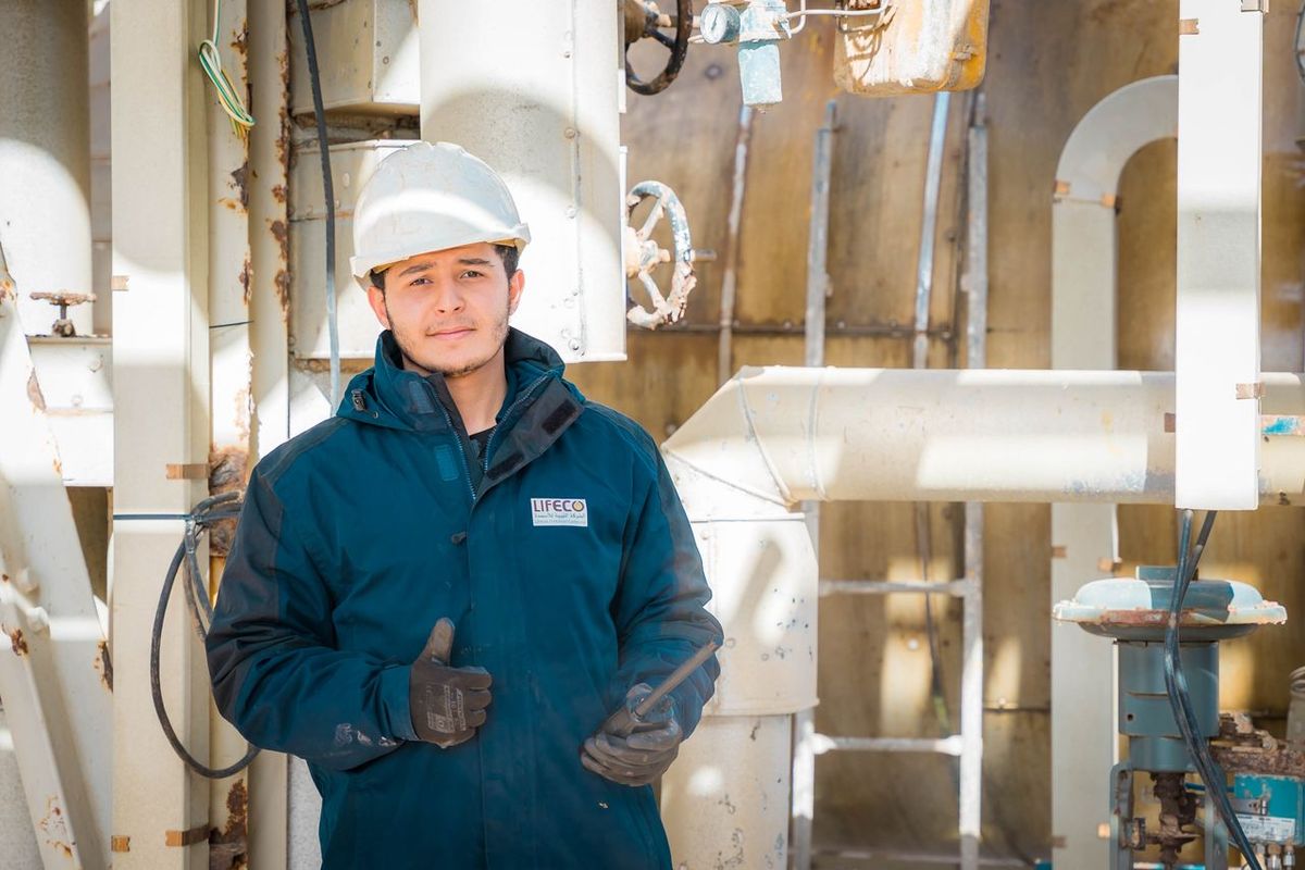 Worker in safety helmet giving thumbs-up in industrial setting.