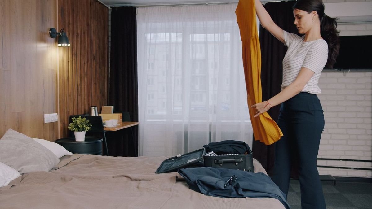 Traveler unpacking clothes from a suitcase in a hotel room.