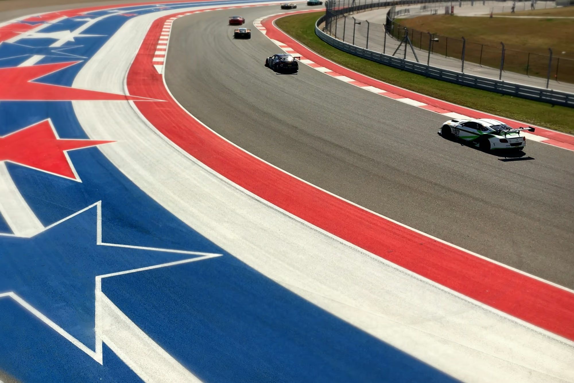 GT race cars sweeping through the red, white, and blue star runoff at Circuit of the Americas