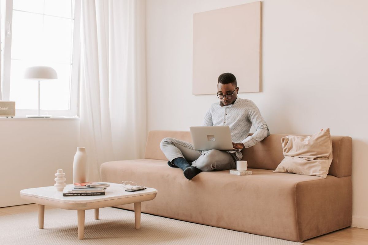 A man using a laptop while sitting on a sofa in a modern, minimalist living room setting.