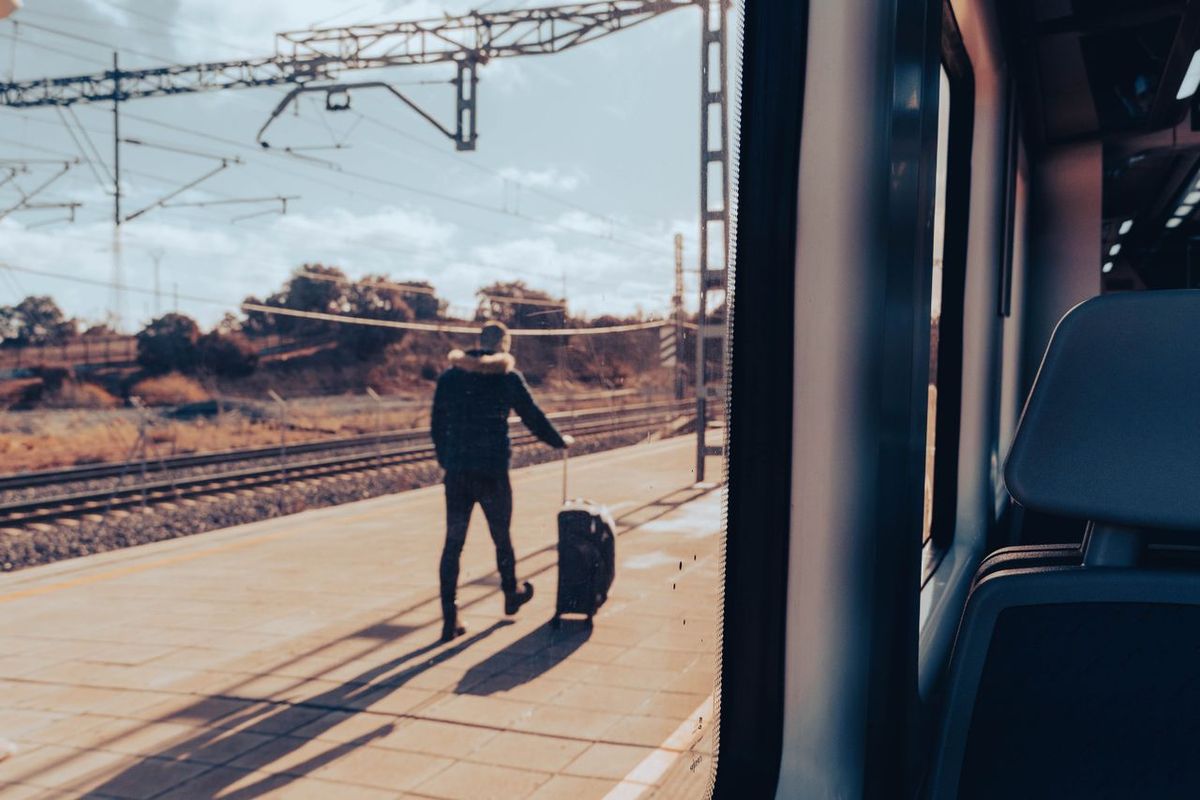 View from a train window of a traveler pulling a suitcase on a station platform.