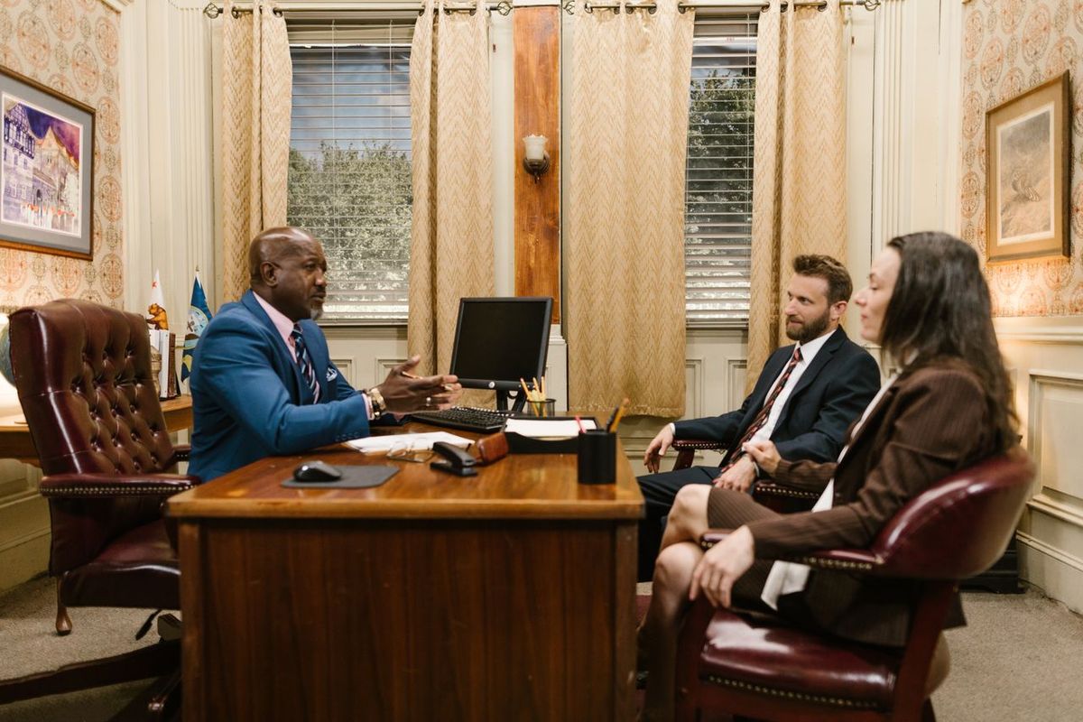 Three people in formal office meeting at desk.