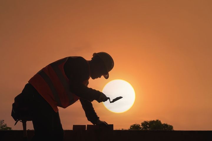 A construction worker silhouetted against a sunset on an active job site
