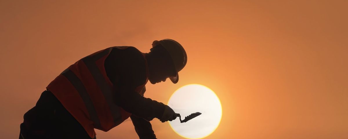 A construction worker silhouetted against a sunset on an active job site