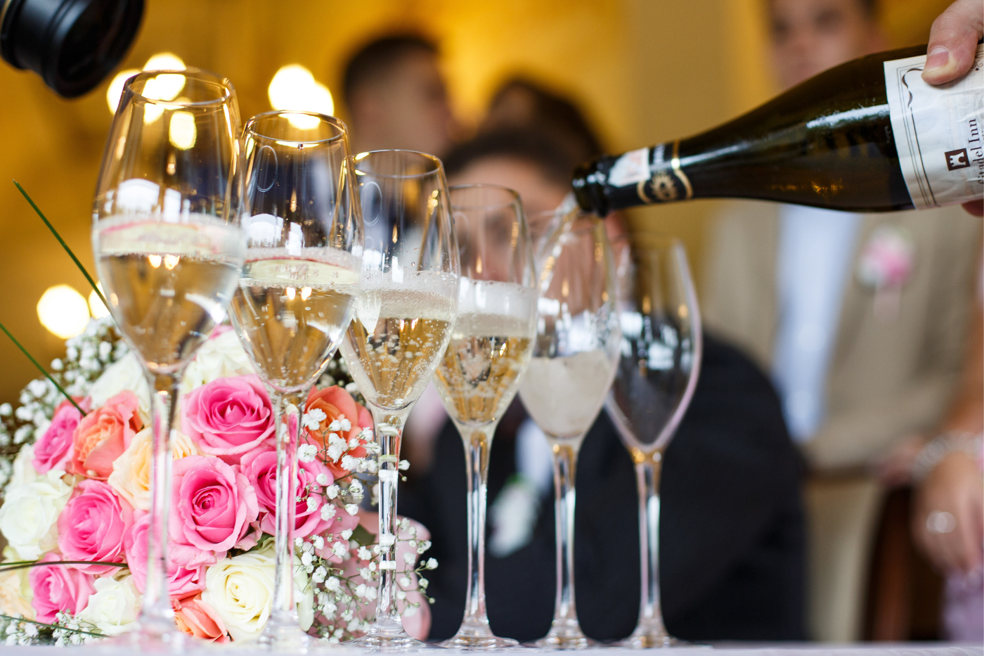 Champagne being poured into glasses beside pink and white flowers at a wedding reception.