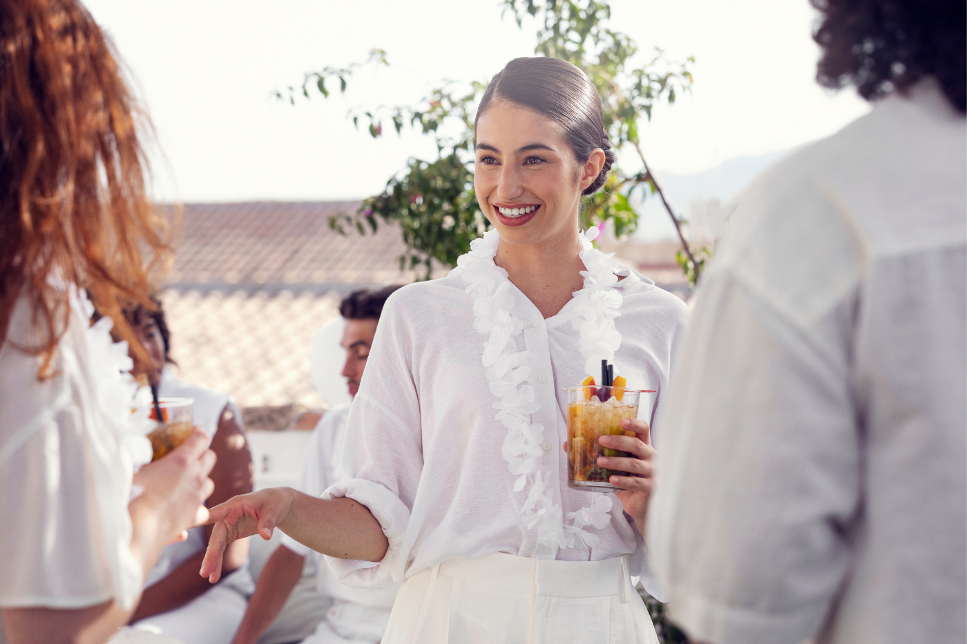 Smiling woman holding a cocktail and talking with guests at an outdoor wedding reception.