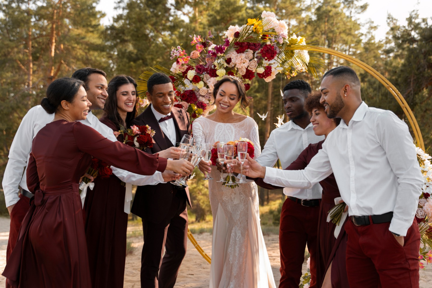 Wedding party raising glasses in a toast during an outdoor ceremony with a colorful floral arch.