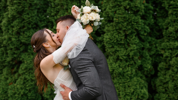 Bride and groom sharing a kiss during wedding photos, bride holding a white peony bouquet