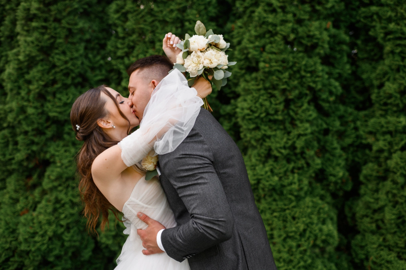 Bride and groom sharing a kiss during wedding photos, bride holding a white peony bouquet