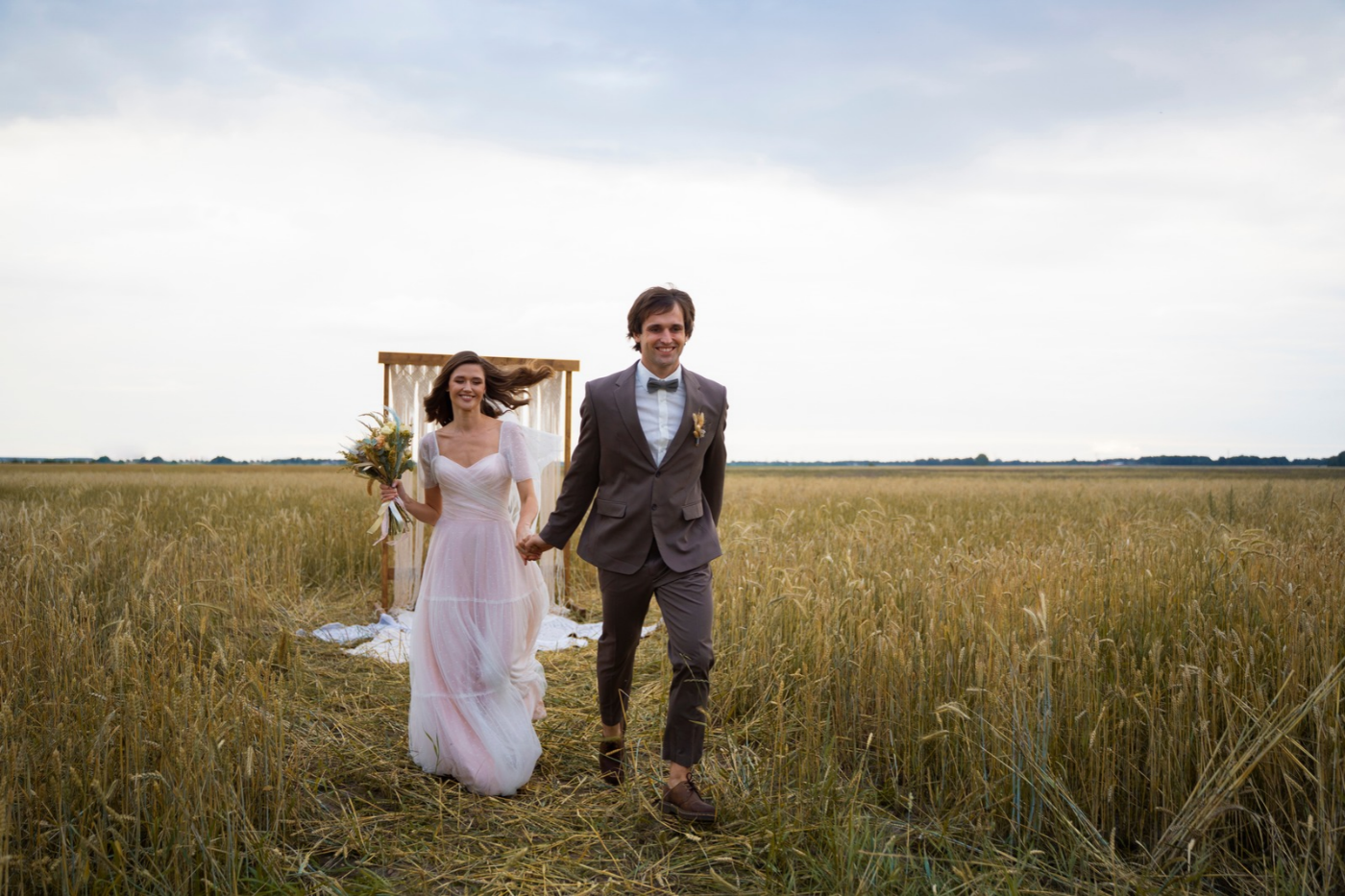 Bride and groom walking through a wheat field after their outdoor wedding ceremony.