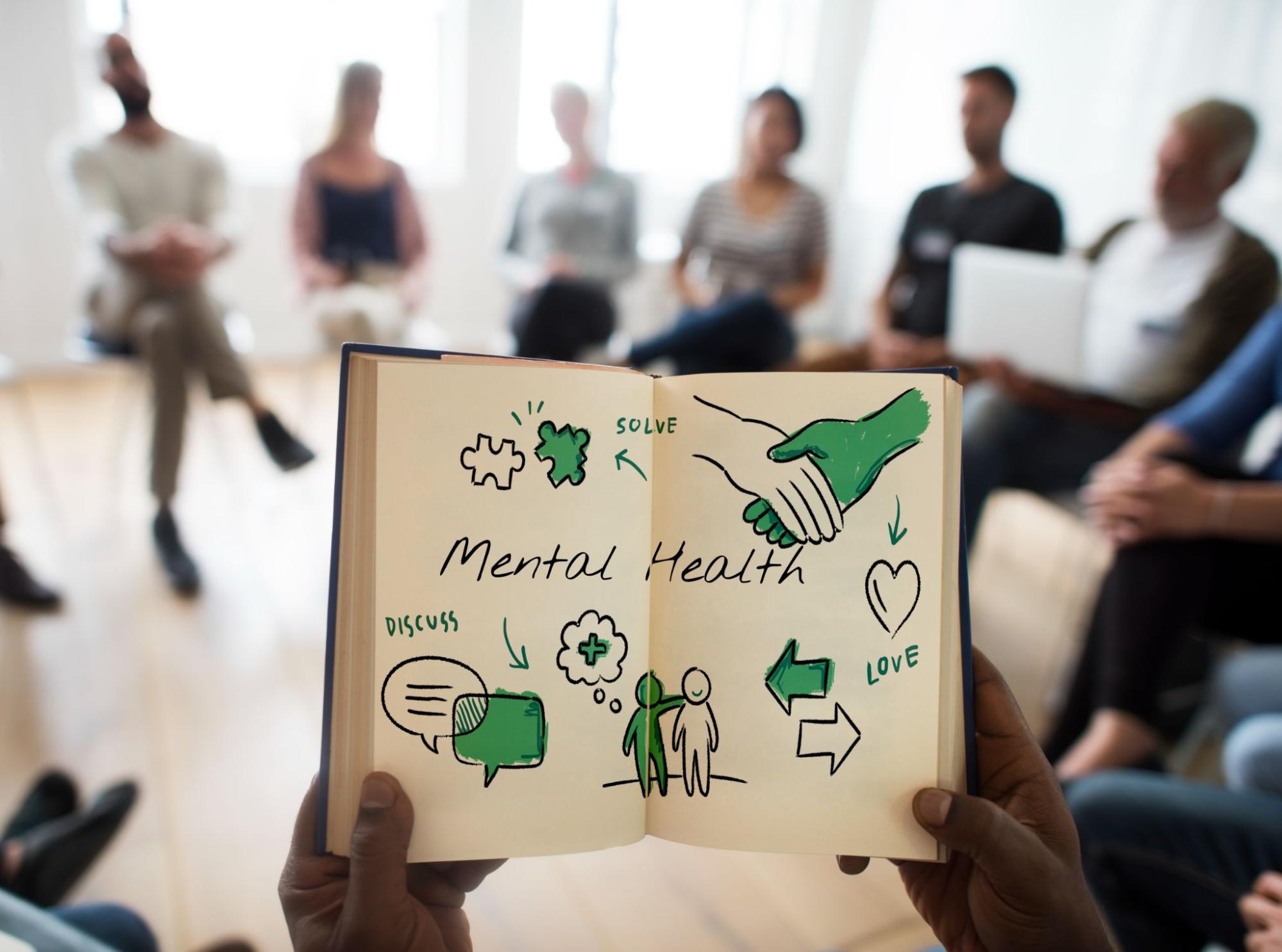 A person holds a book featuring a drawing that represents mental health awareness and support.