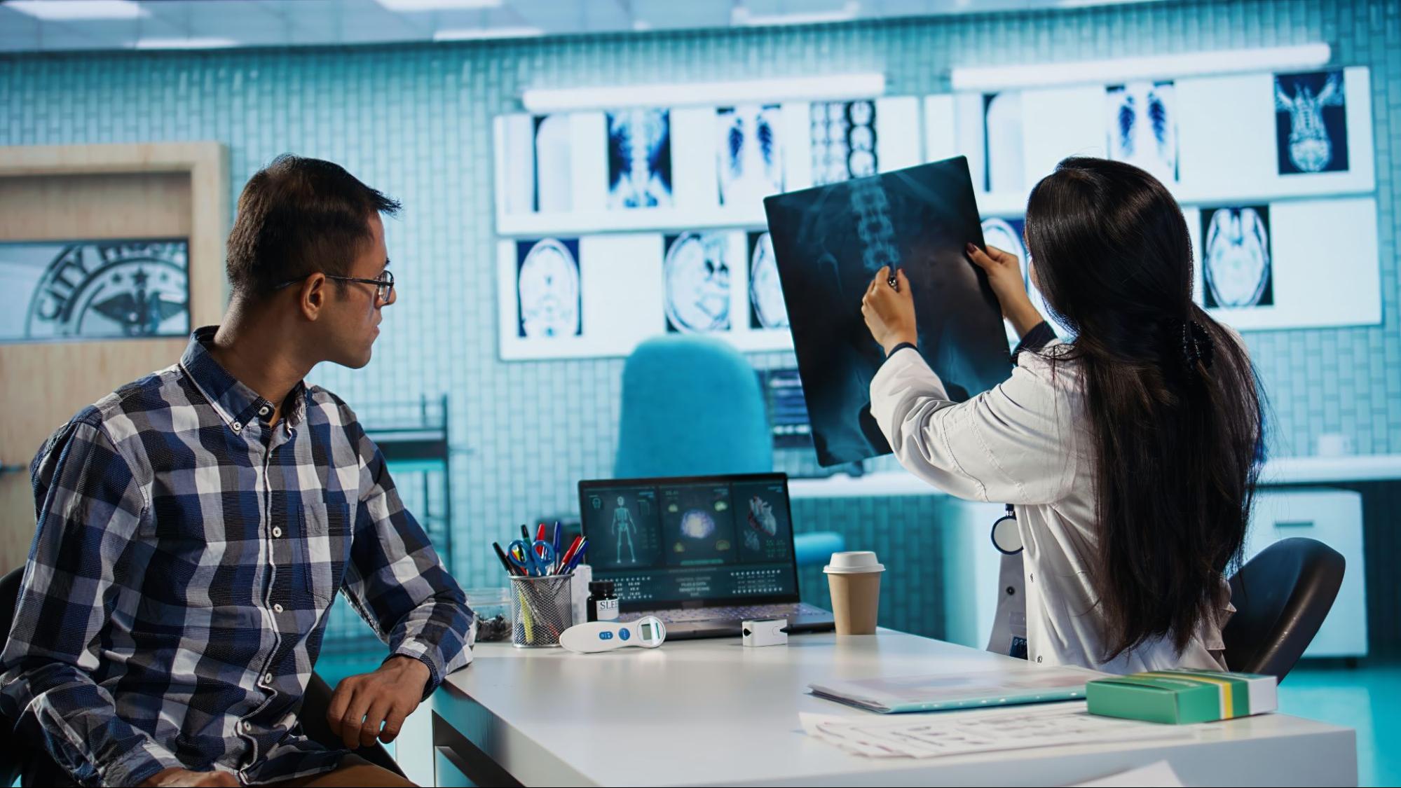 A man and woman examine an x-ray together in a hospital room, discussing the medical image.