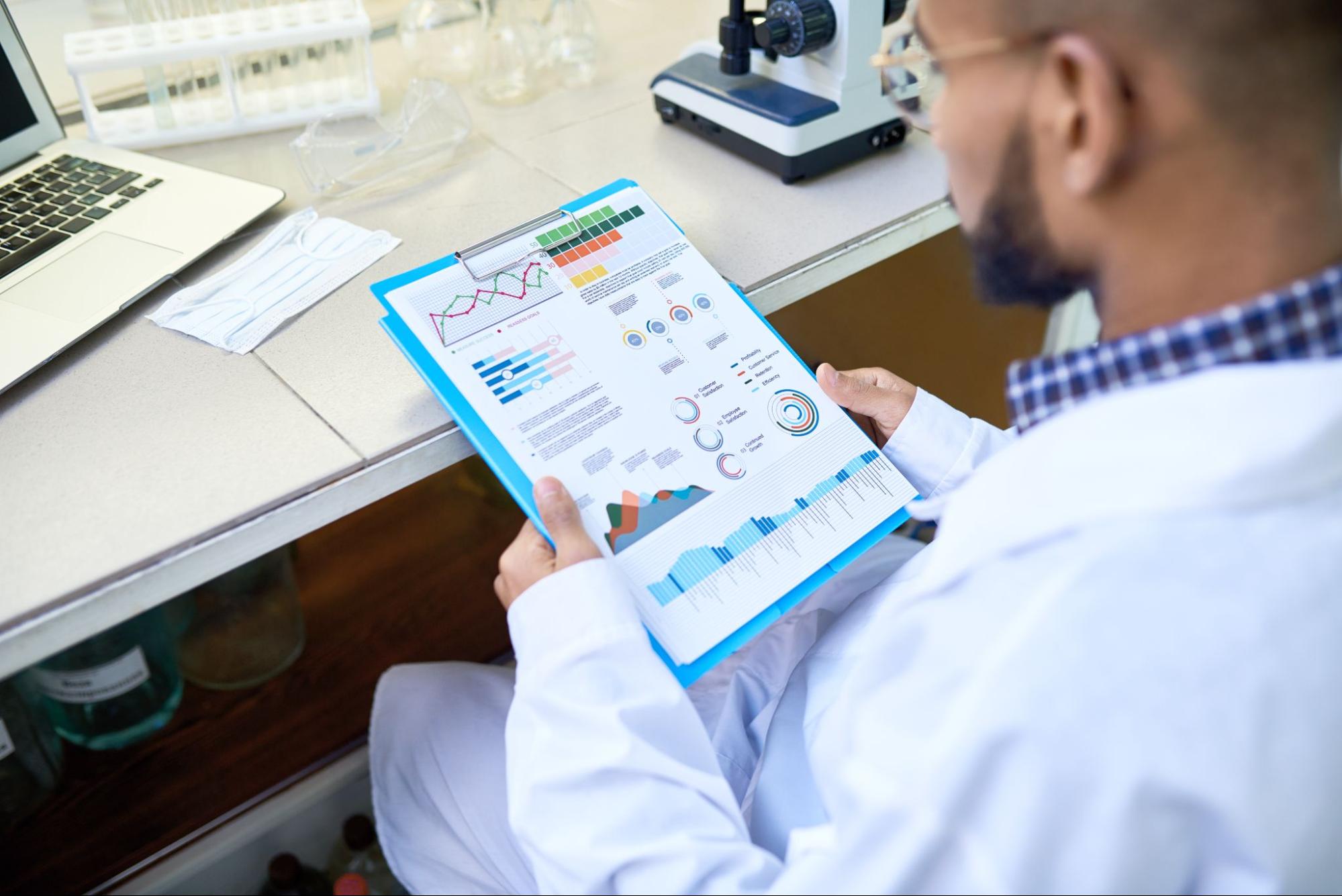 A man in a lab coat examines a chart, analyzing data in a laboratory setting.