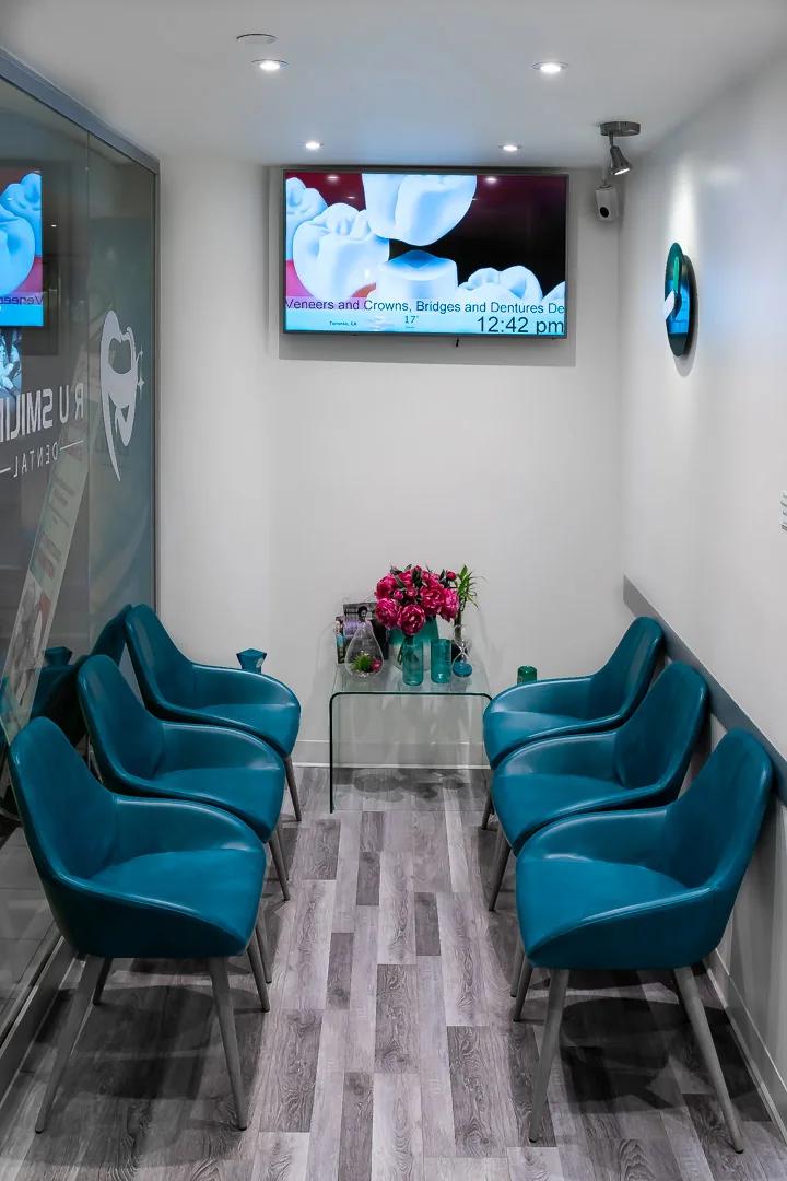 The waiting room: six teal upholstered chairs along the wall, a wall-mounted screen and fresh flowers