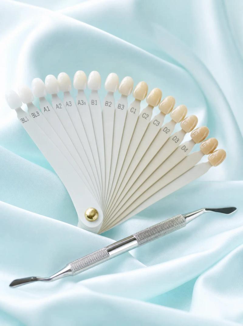 A porcelain shade guide and a restorative hand instrument on pale aqua silk