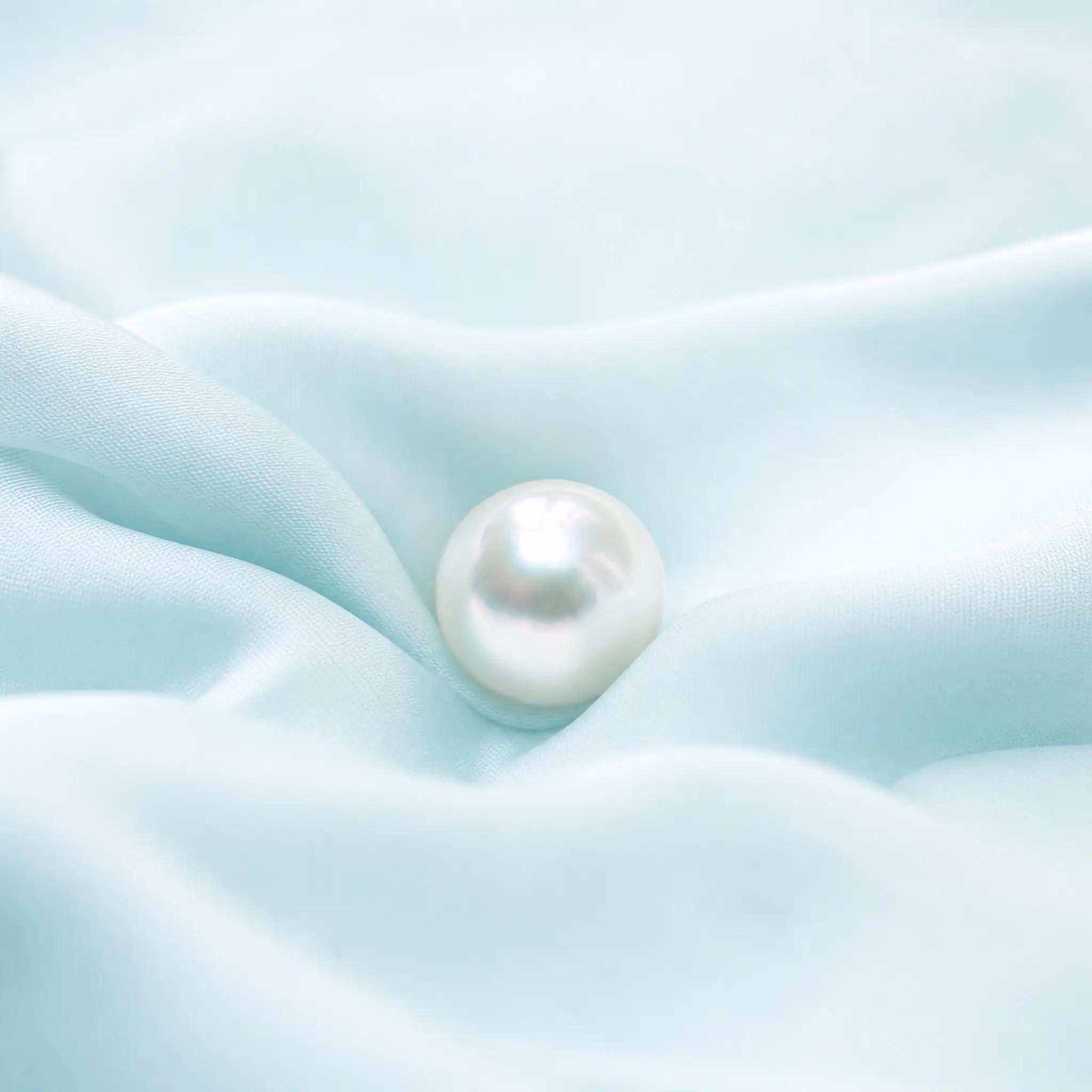 An iridescent pearl resting on pale aqua silk