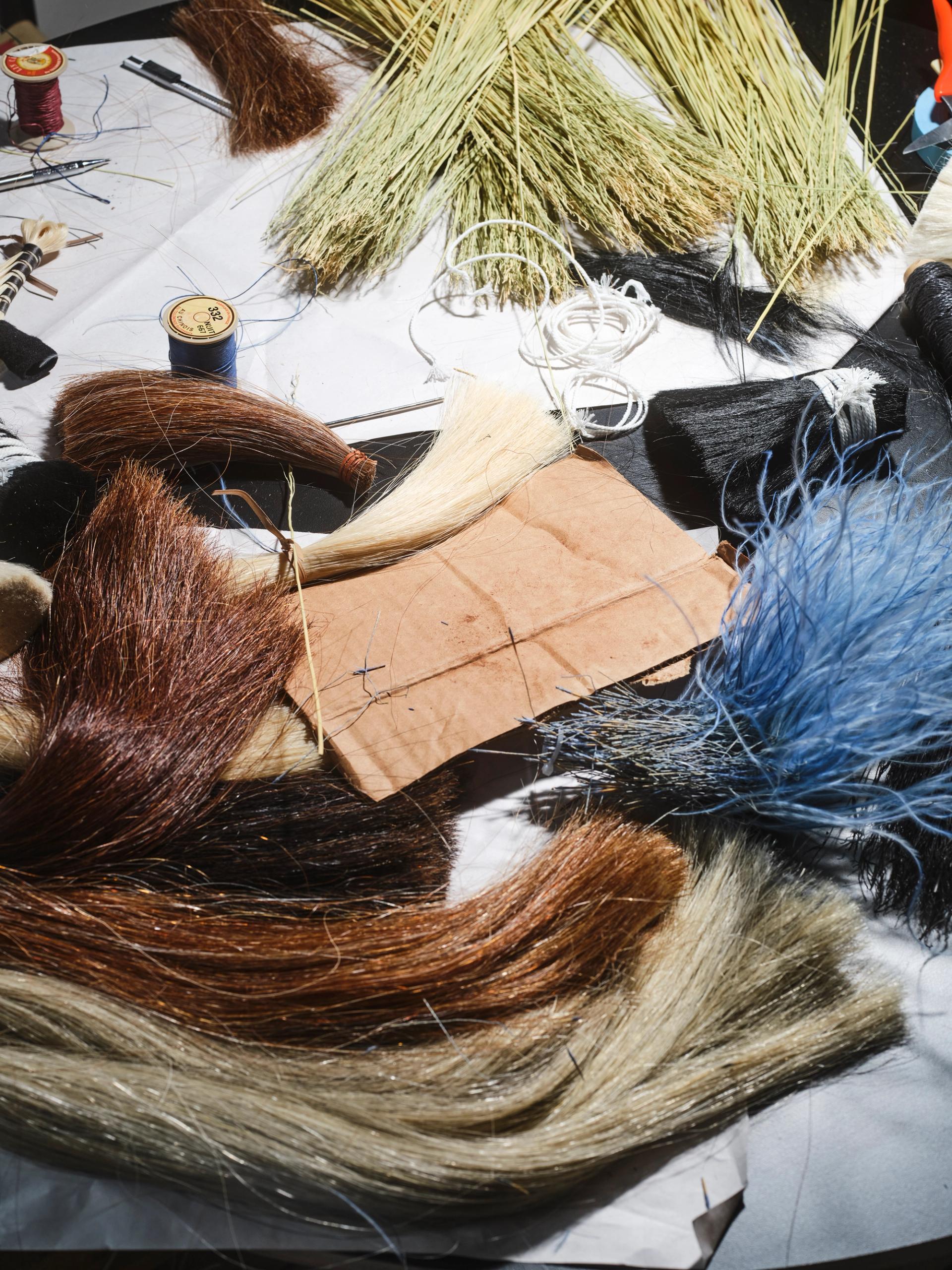 Broom-making materials and tools scattered on a work surface, including fibers, thread, and bundles of reeds.