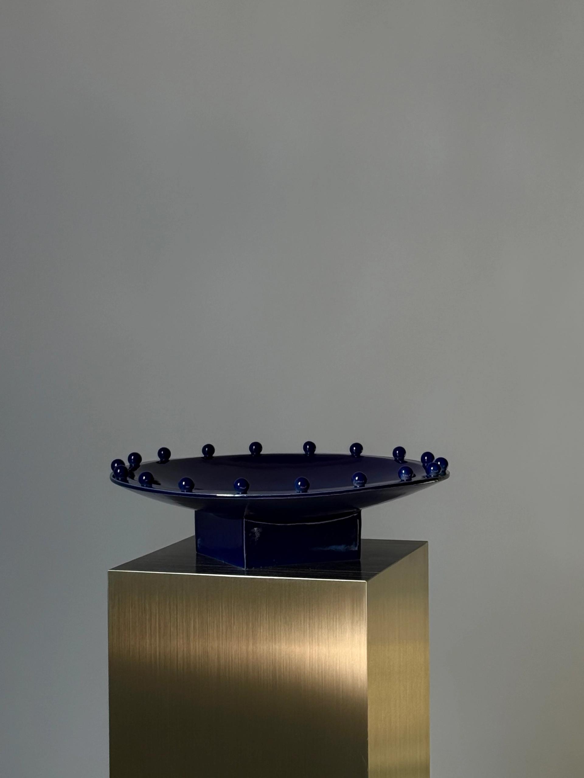 Blue ceramic plate on a gold plinth against gray backdrop.