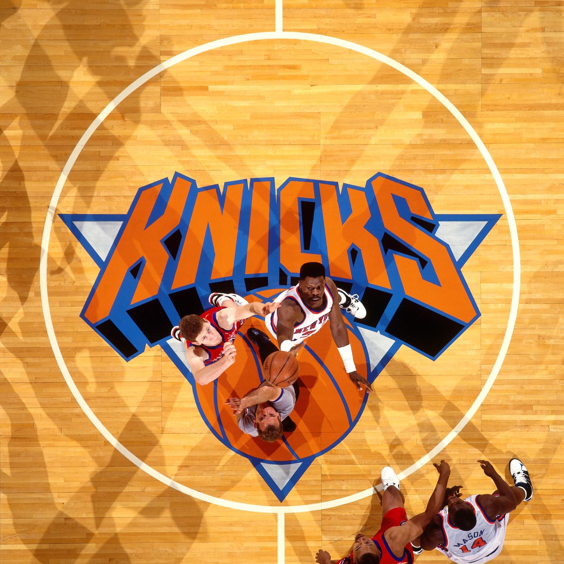 Overhead view of a basketball tip-off at center court above the New York Knicks logo.