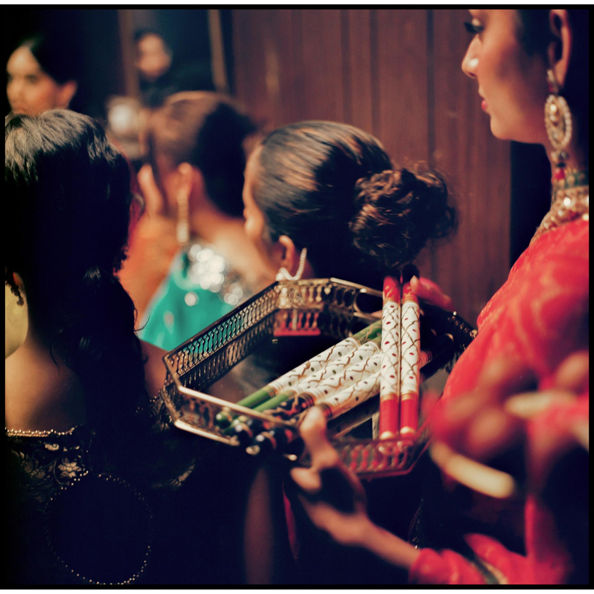 A close-up of performers in South Asian attire passing an ornate tray holding decorated bangles and ceremonial objects