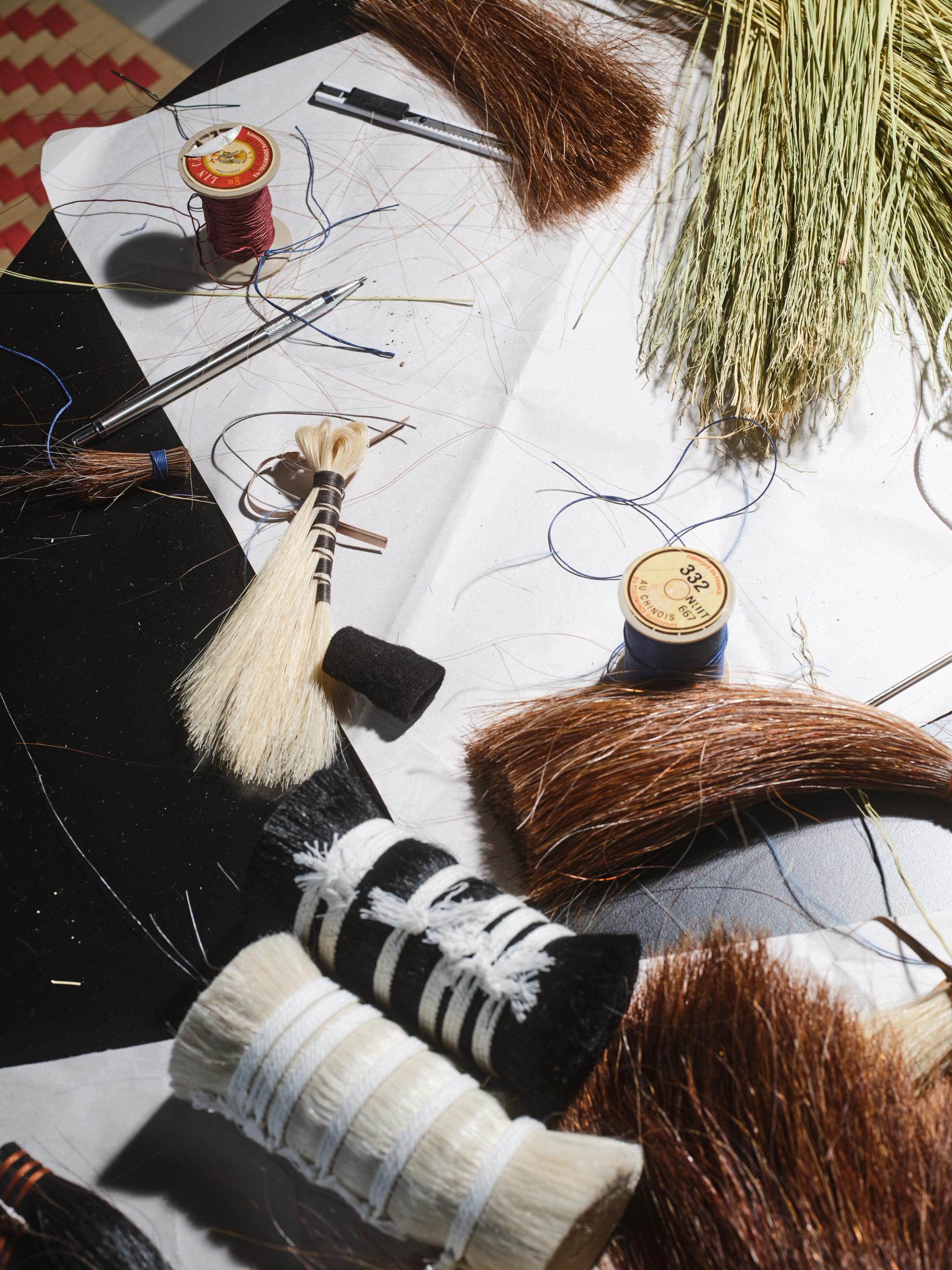 Broom-making materials and tools scattered on a work surface, including fibers, thread, and small brushes.