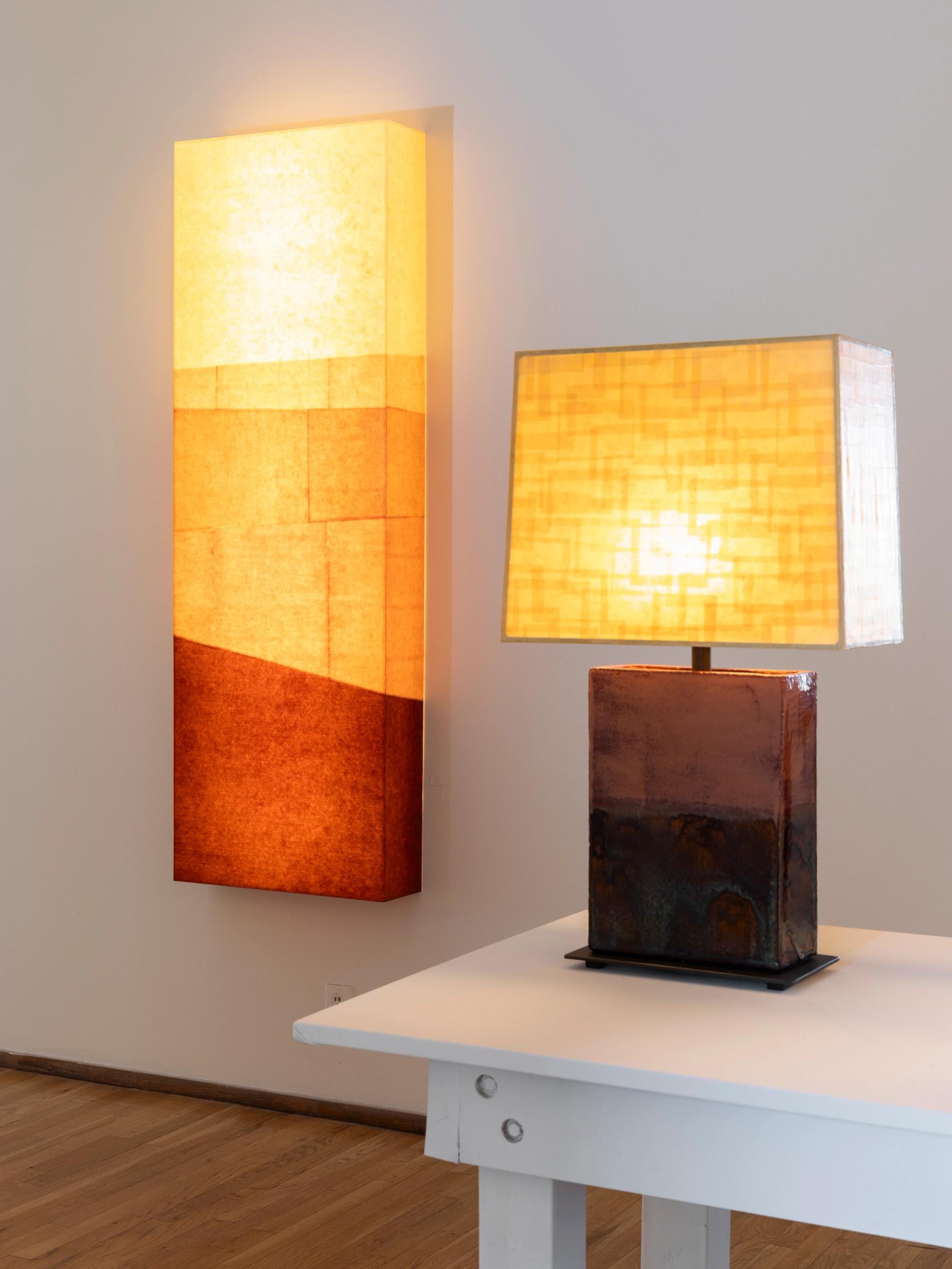 Illuminated geometric wall sculpture and ceramic lamp glowing in warm amber tones.