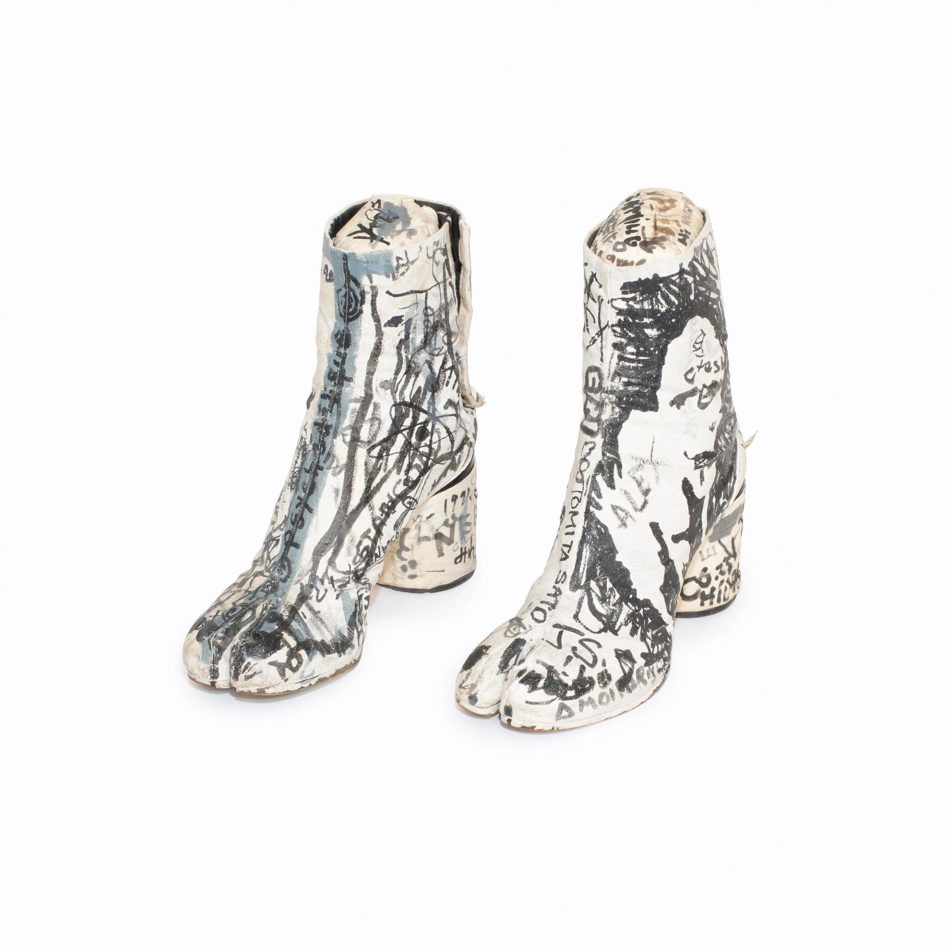 Pair of white split-toe ankle boots covered in black hand-drawn graffiti-style illustrations and handwritten text.