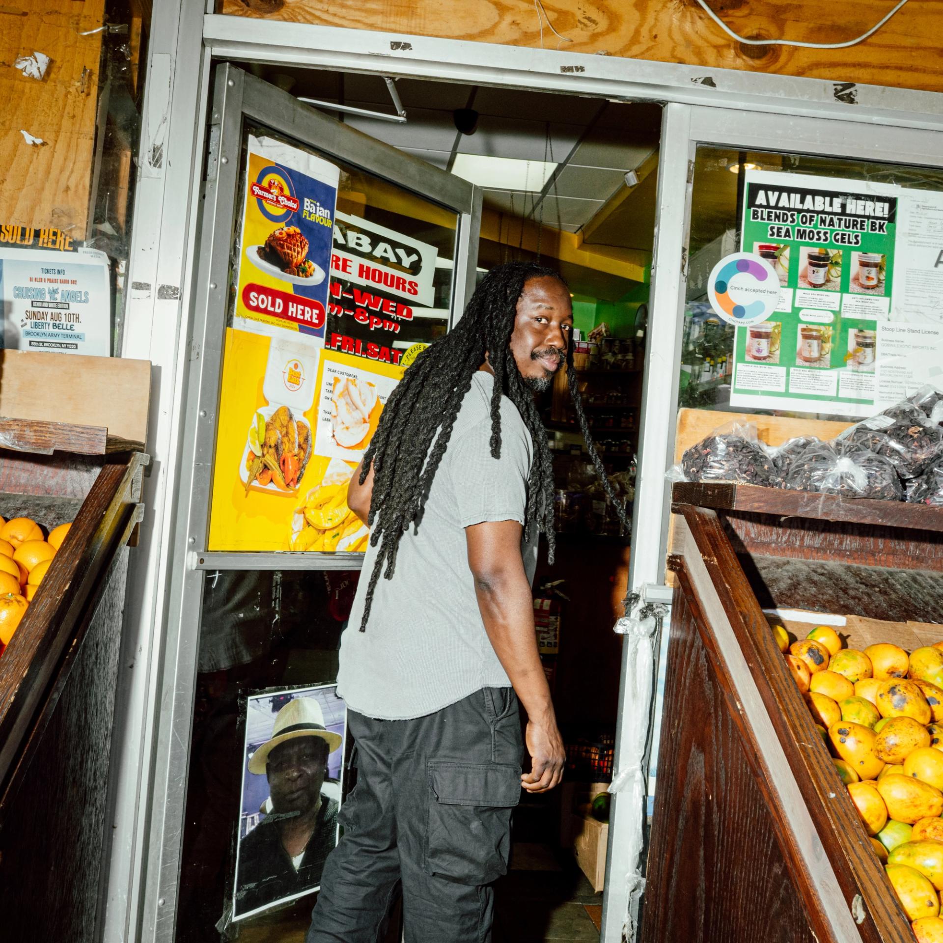 Portrait of a man entering a store, standing among boxes of oranges.