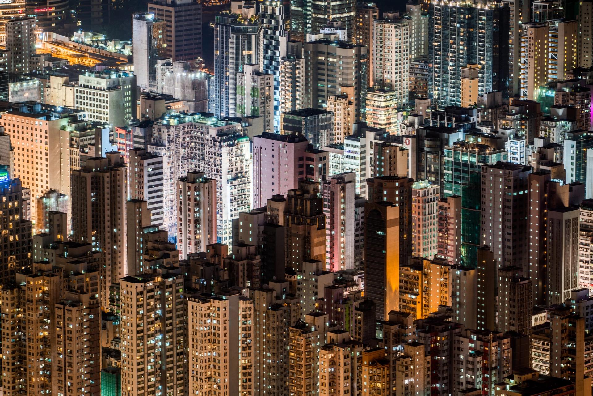 Dense high-rise buildings at night, windows glowing across a crowded Hong Kong city skyline.