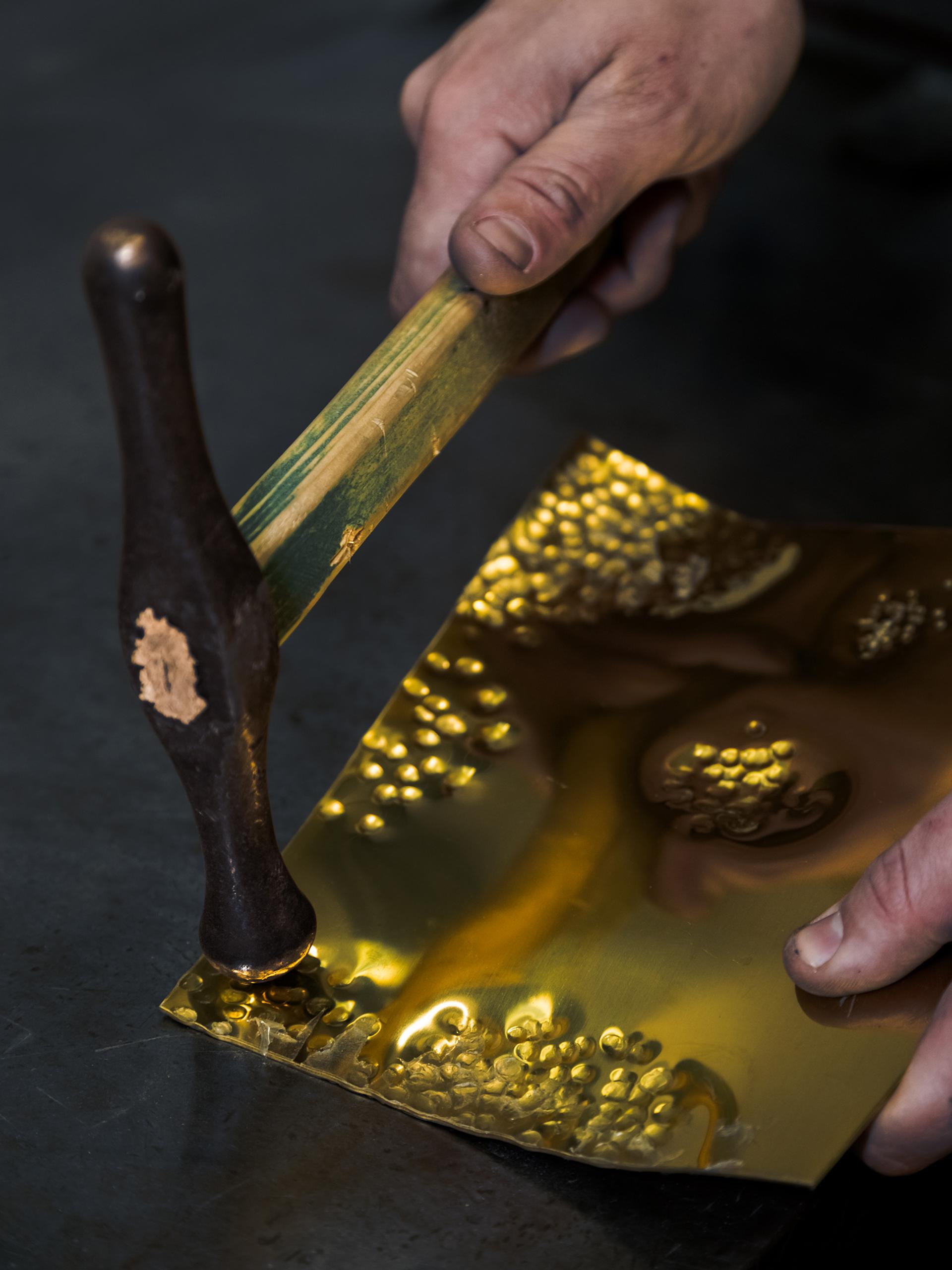 Close-up photo of a hand hammering a sheet of gold foil.