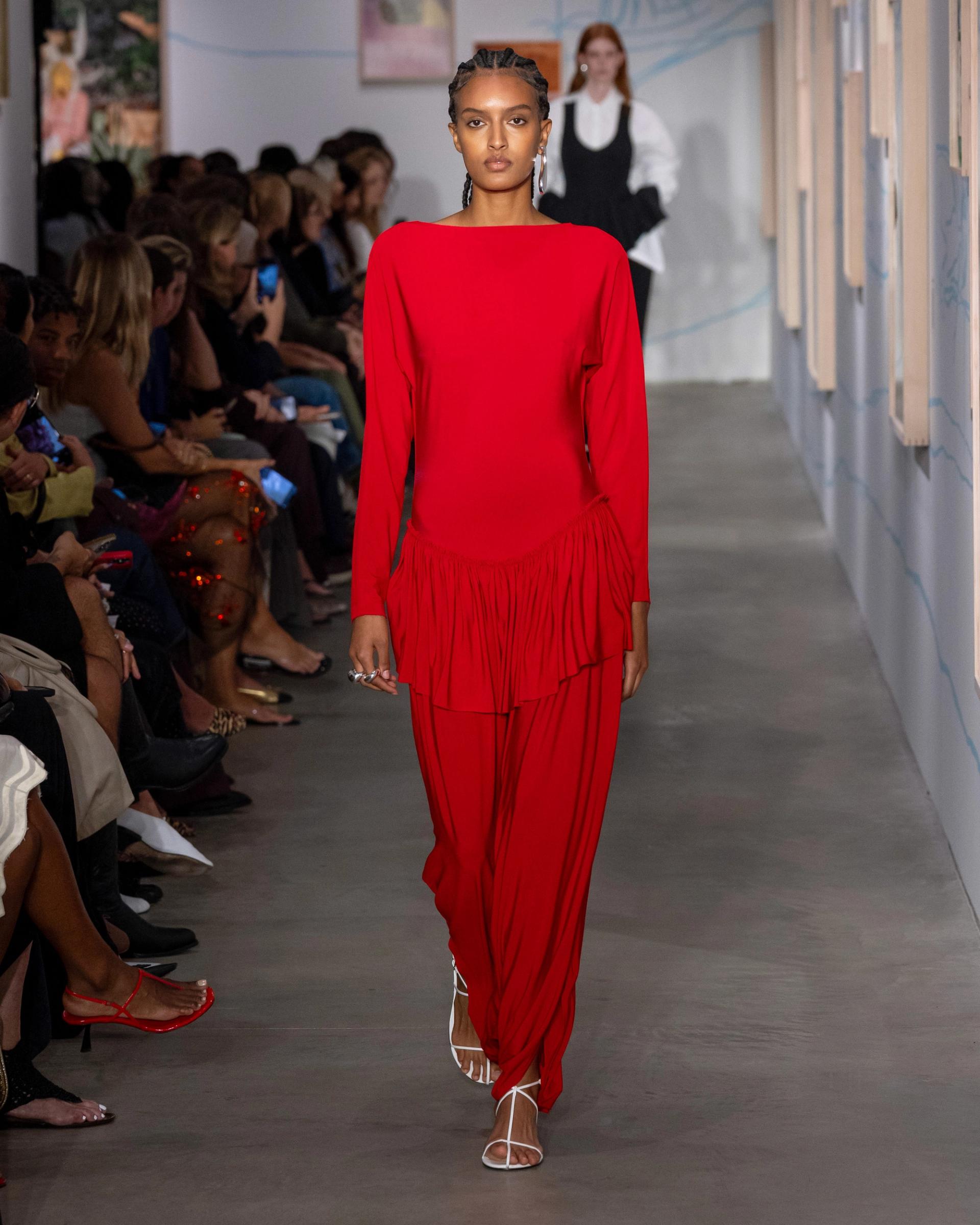 A model walks a runway wearing an all-red ensemble with a drop waist with ruffled hem and flowy pants