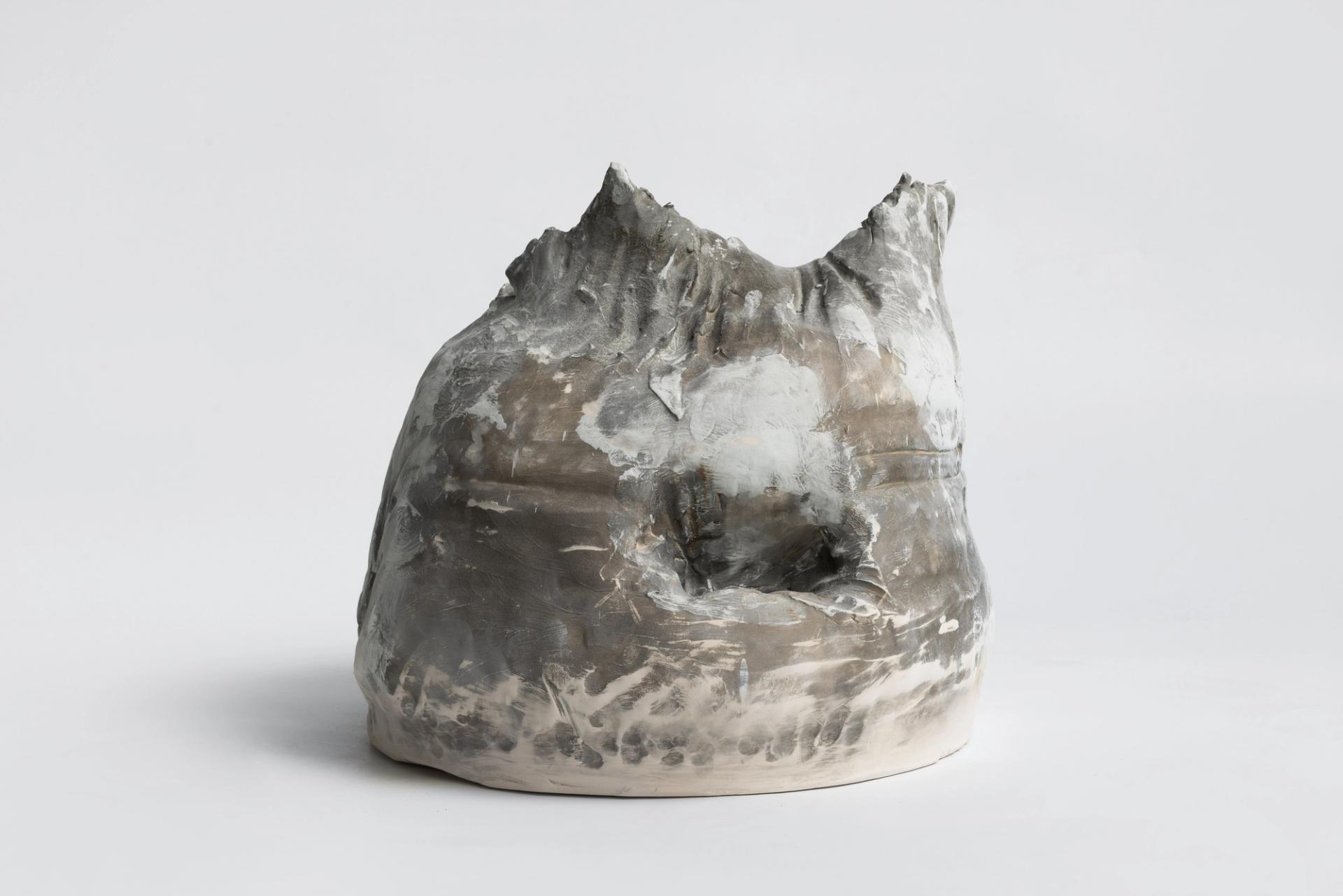 Rough-hewn gray ceramic vessel with a jagged rim and crater-like opening, marked by smoky, ash-toned surfaces.