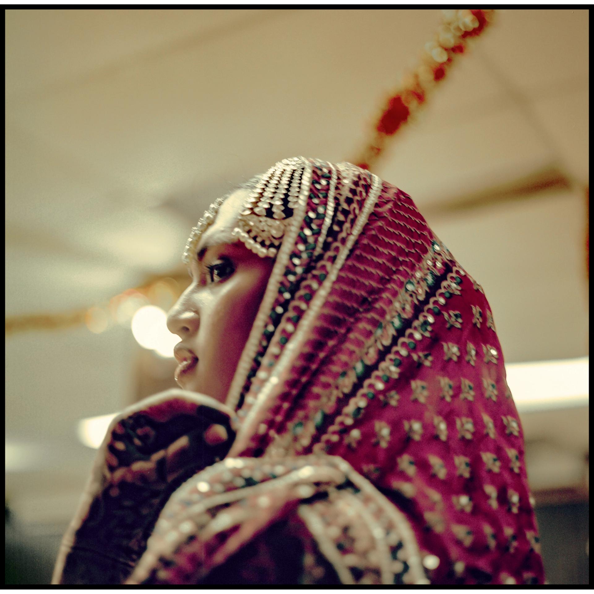A close-up portrait of a performer in an embroidered burgundy dupatta gazing upward against a softly lit background