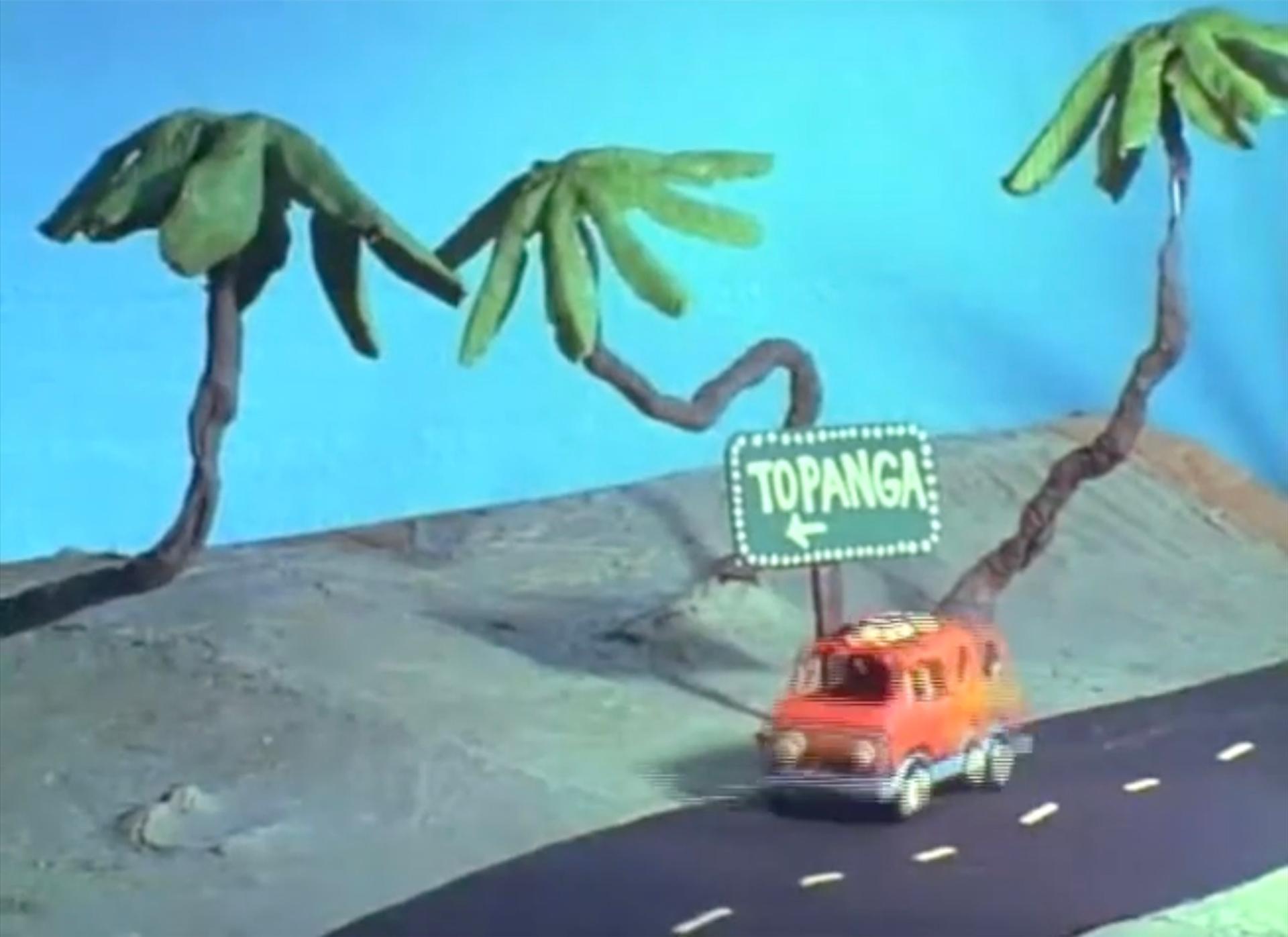 Stop-motion animation still of a claymation orange van driving down a road past stylized palm trees, beneath a green road sign reading "Topanga" with a left-pointing arrow.