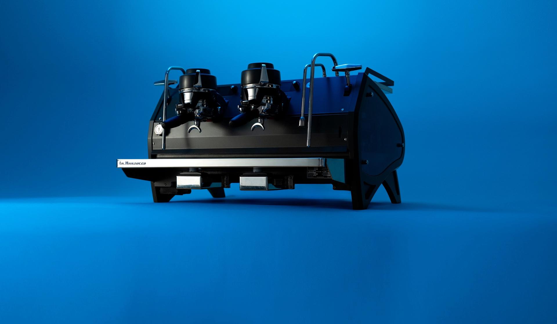 A La Marzocco two-group espresso machine in matte black, photographed against a vivid blue studio background.