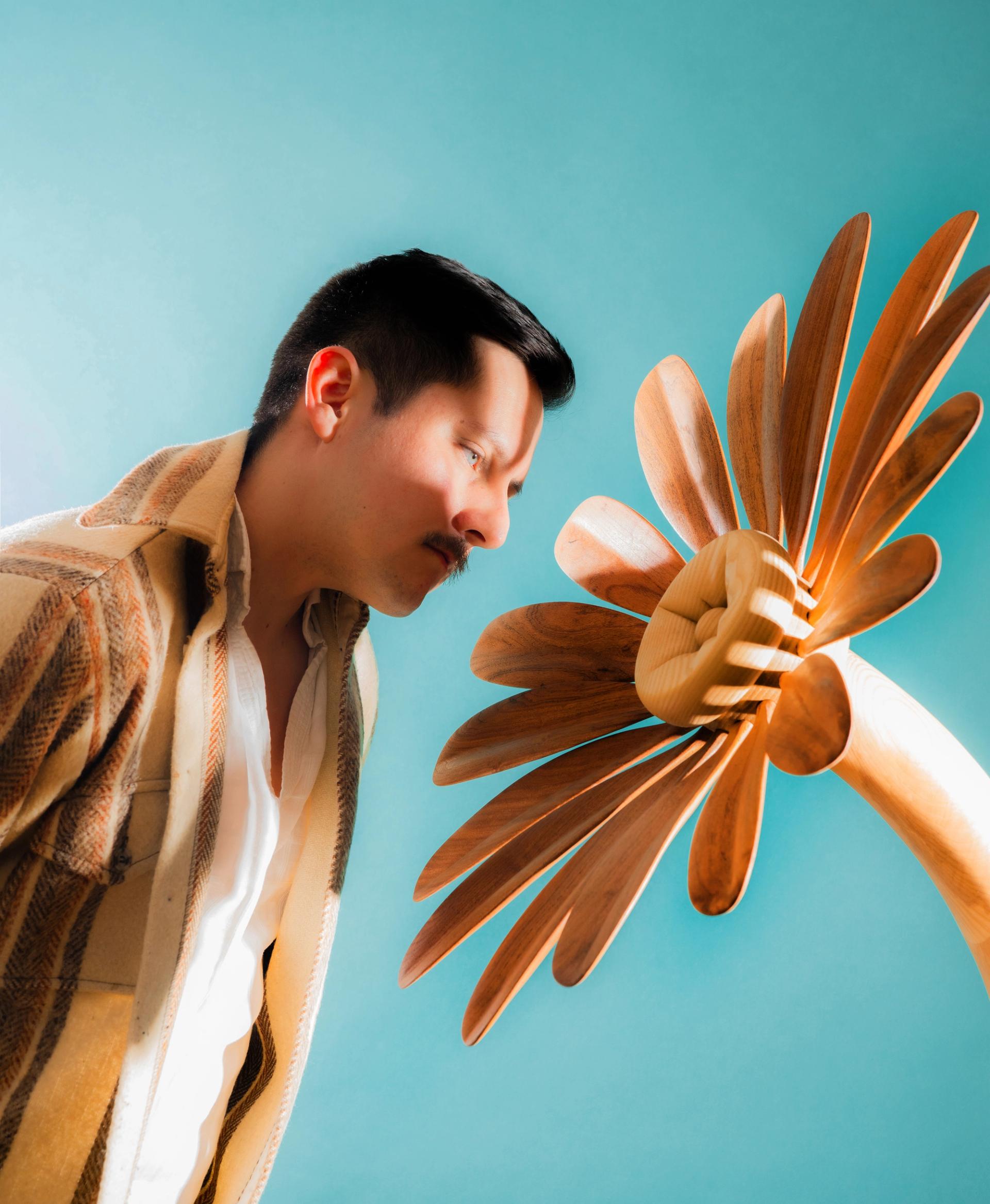 A man seen in profile looks closely at a large wooden flower shape against a light blue background.