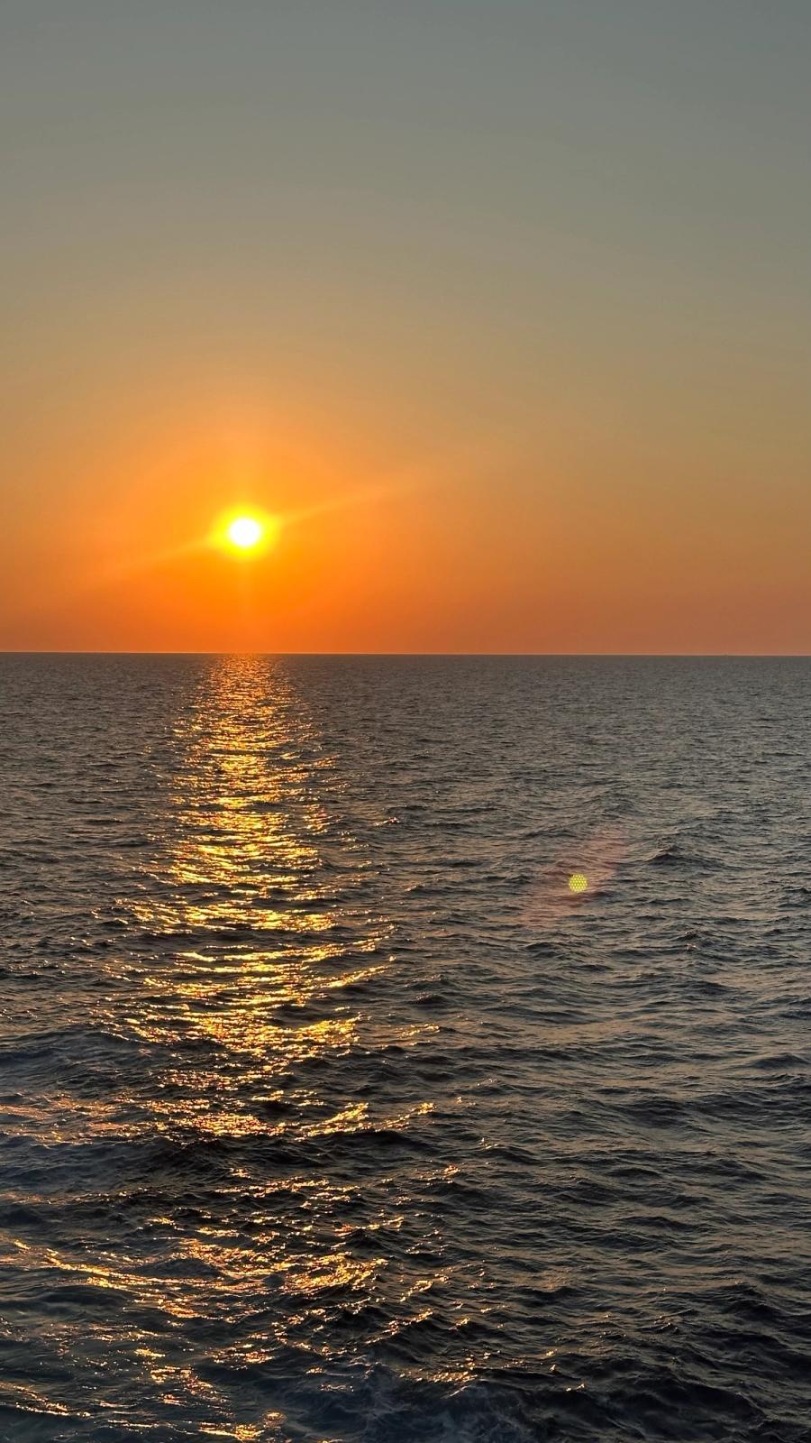Pôr do sol sobre o mar, com o reflexo dourado da luz sobre a água.
