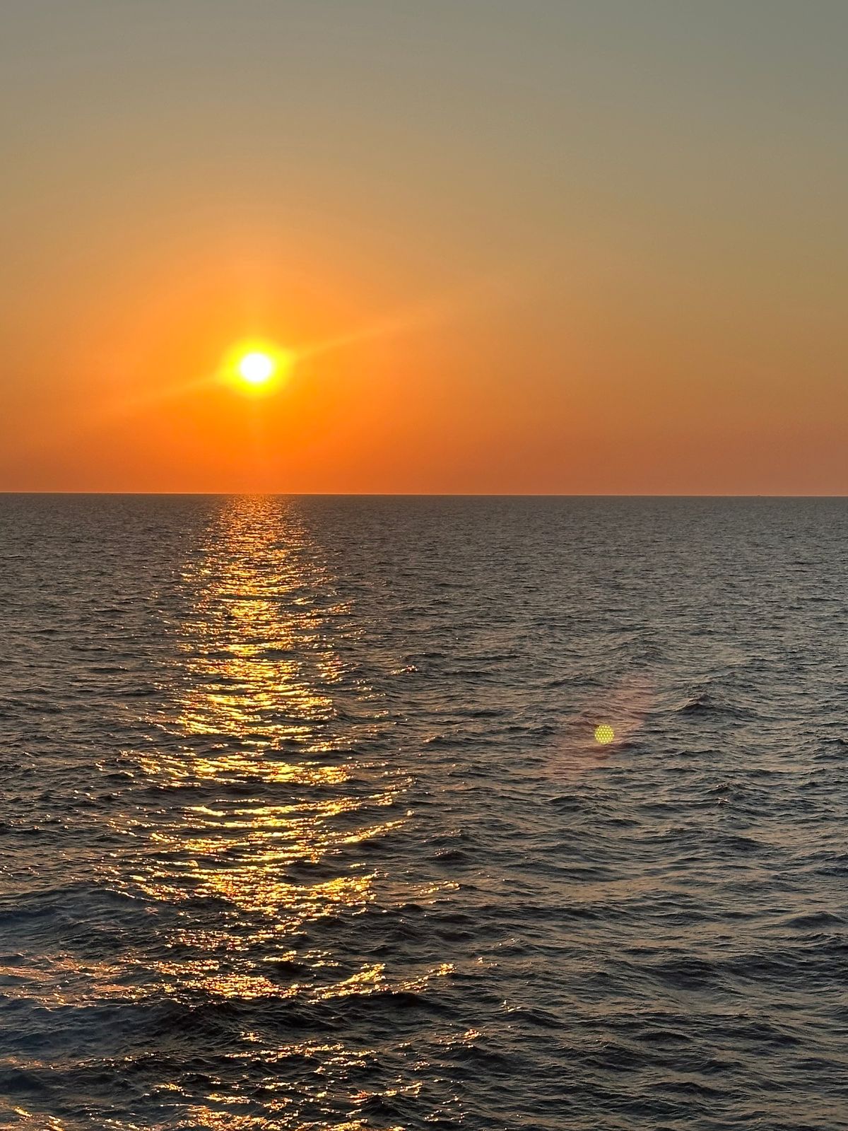 Pôr do sol sobre o mar, com o reflexo dourado da luz sobre a água.