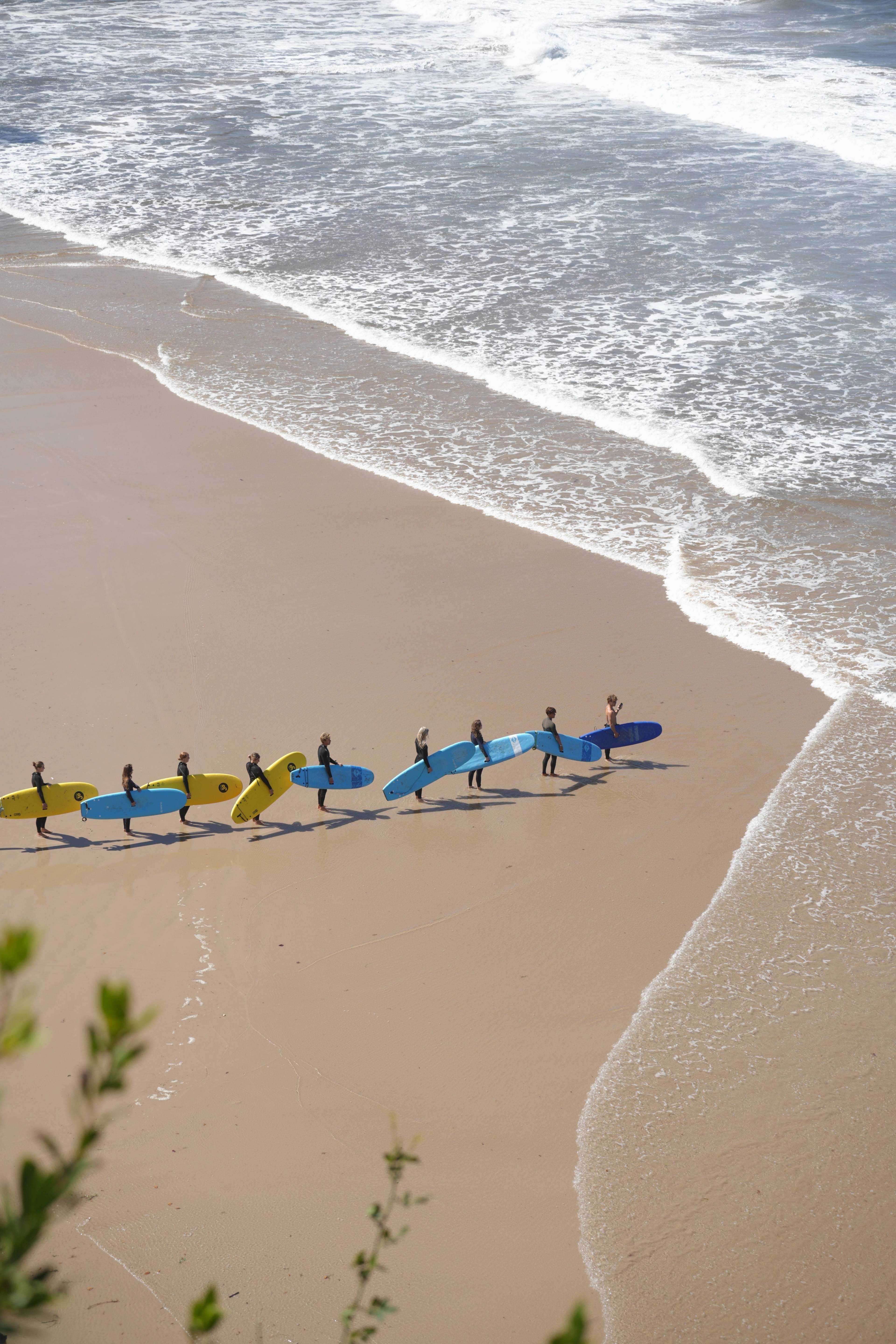 A line of surfers walking down the beach toward the white water, colourful boards under-arm