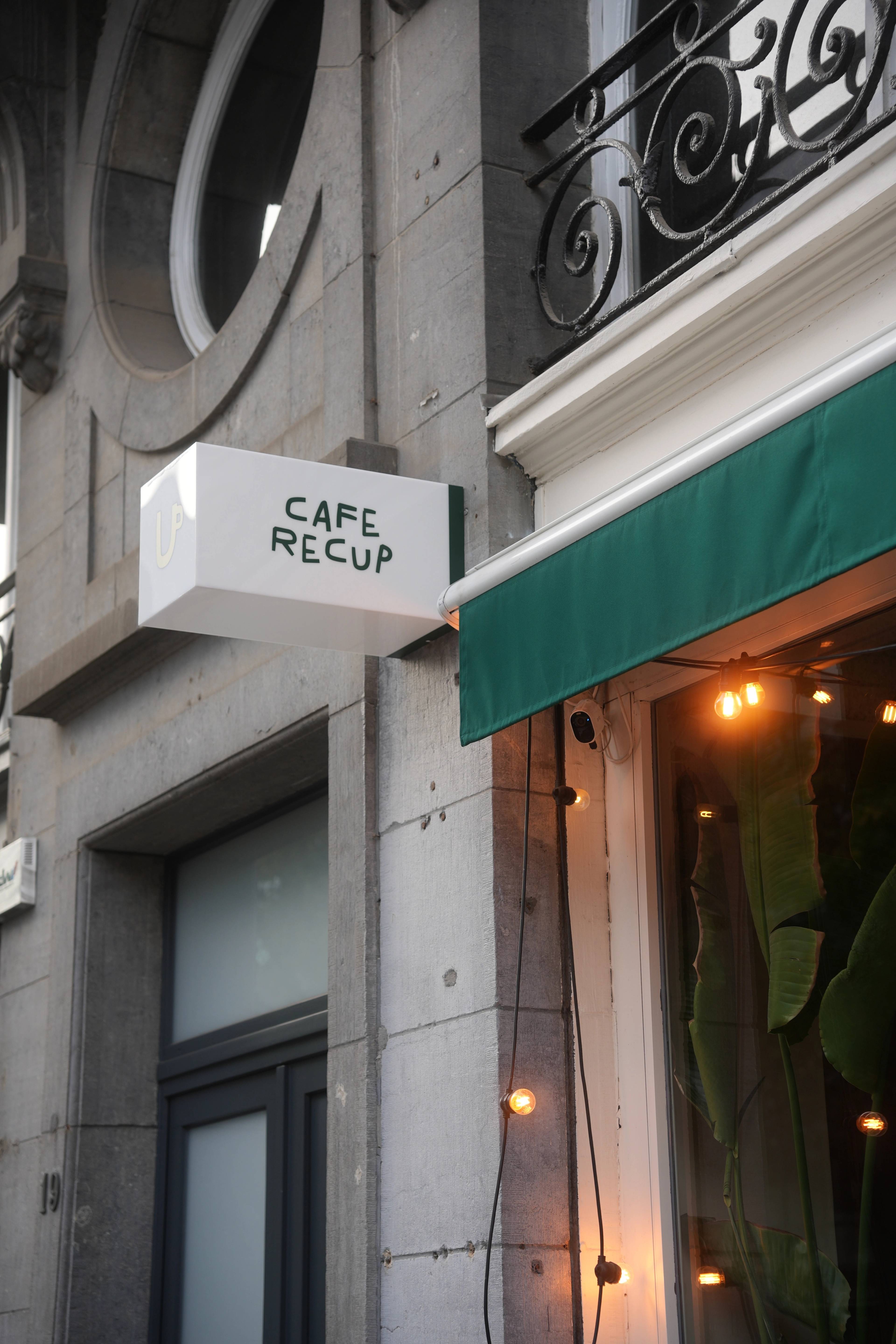 Café Recup sign lit under wrought-iron balconies, fairy lights below