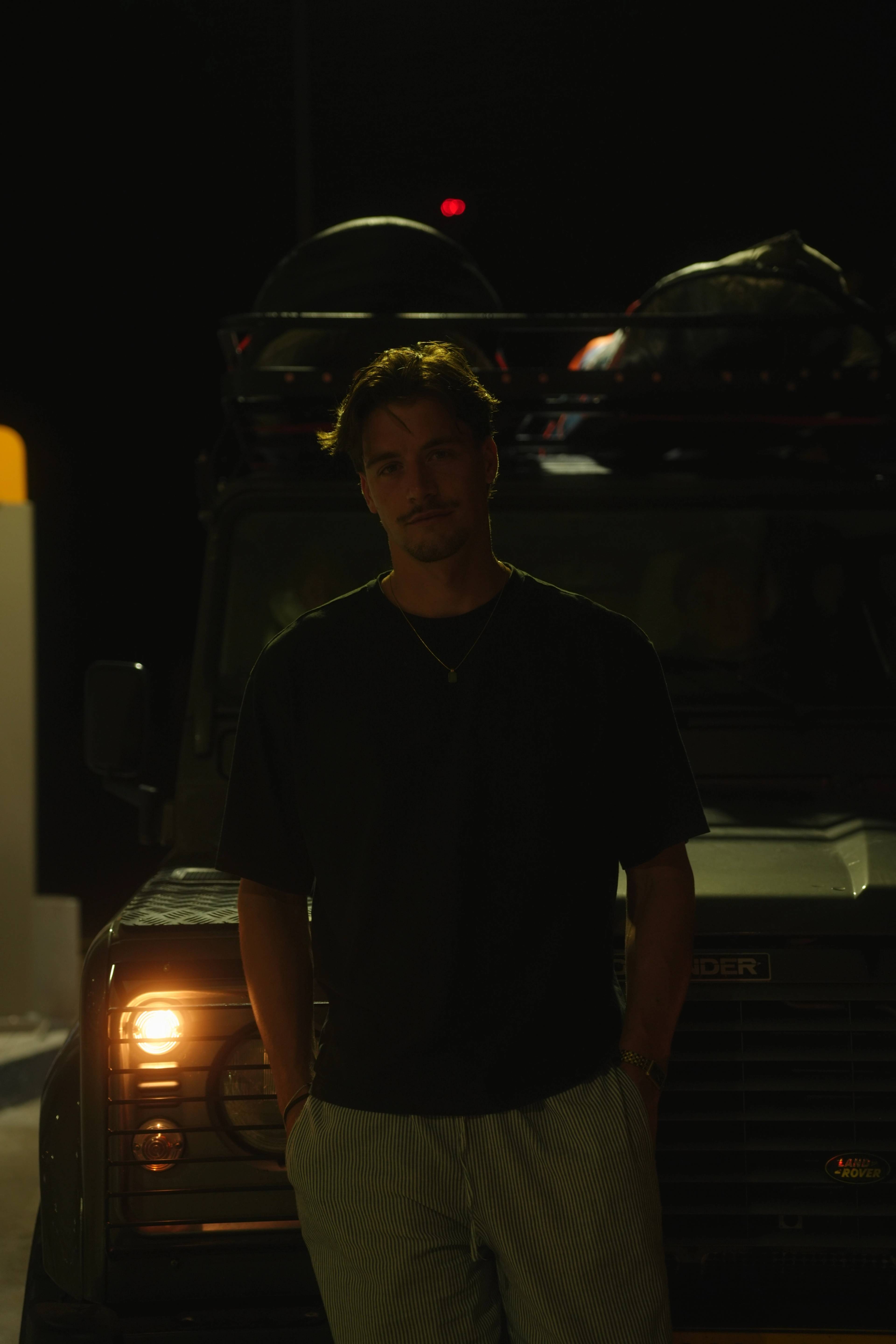 Back at the Landrover at night, leaning on the front grille, headlight low