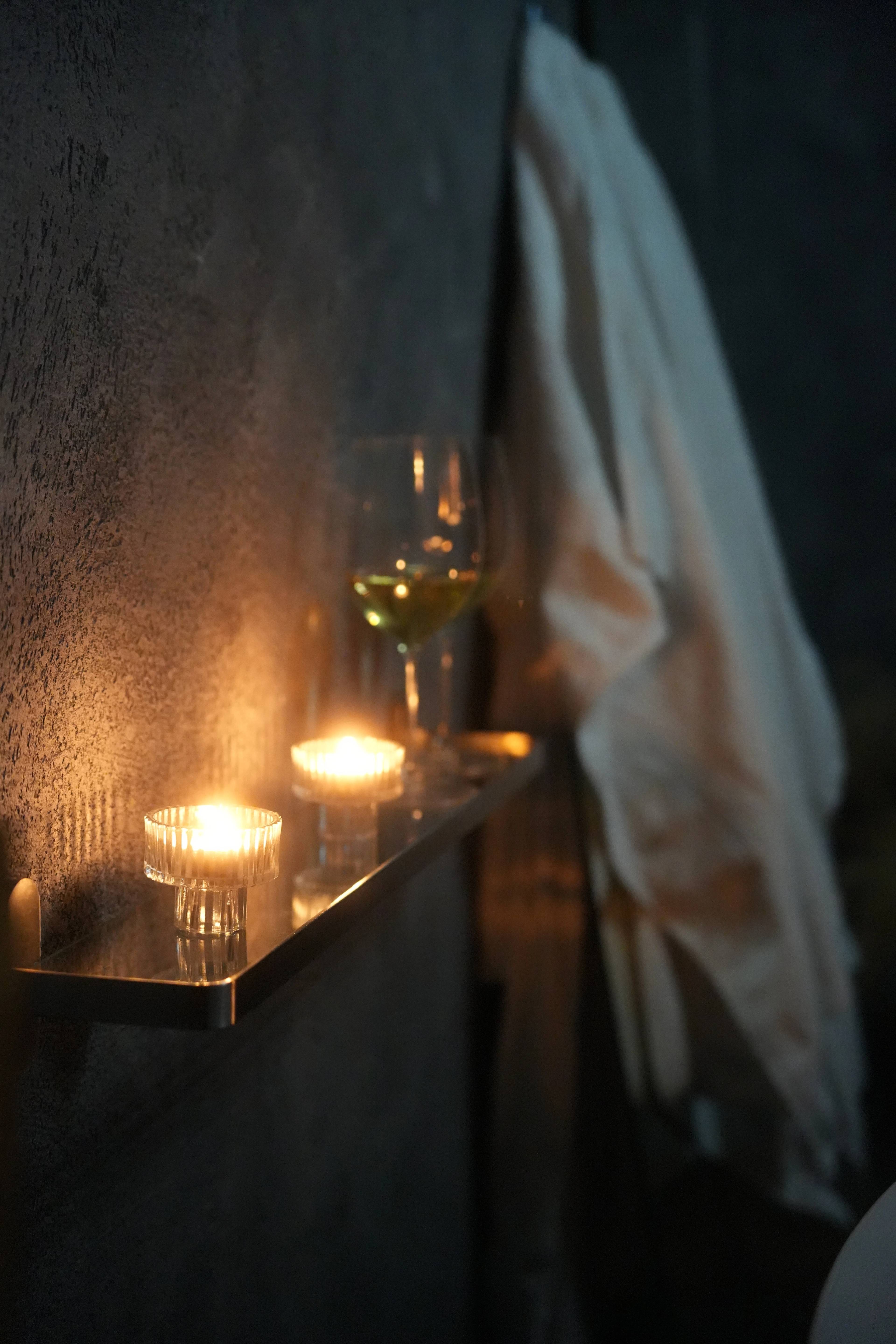 Tea lights and a glass of white wine on a brass shelf, robe hanging beside
