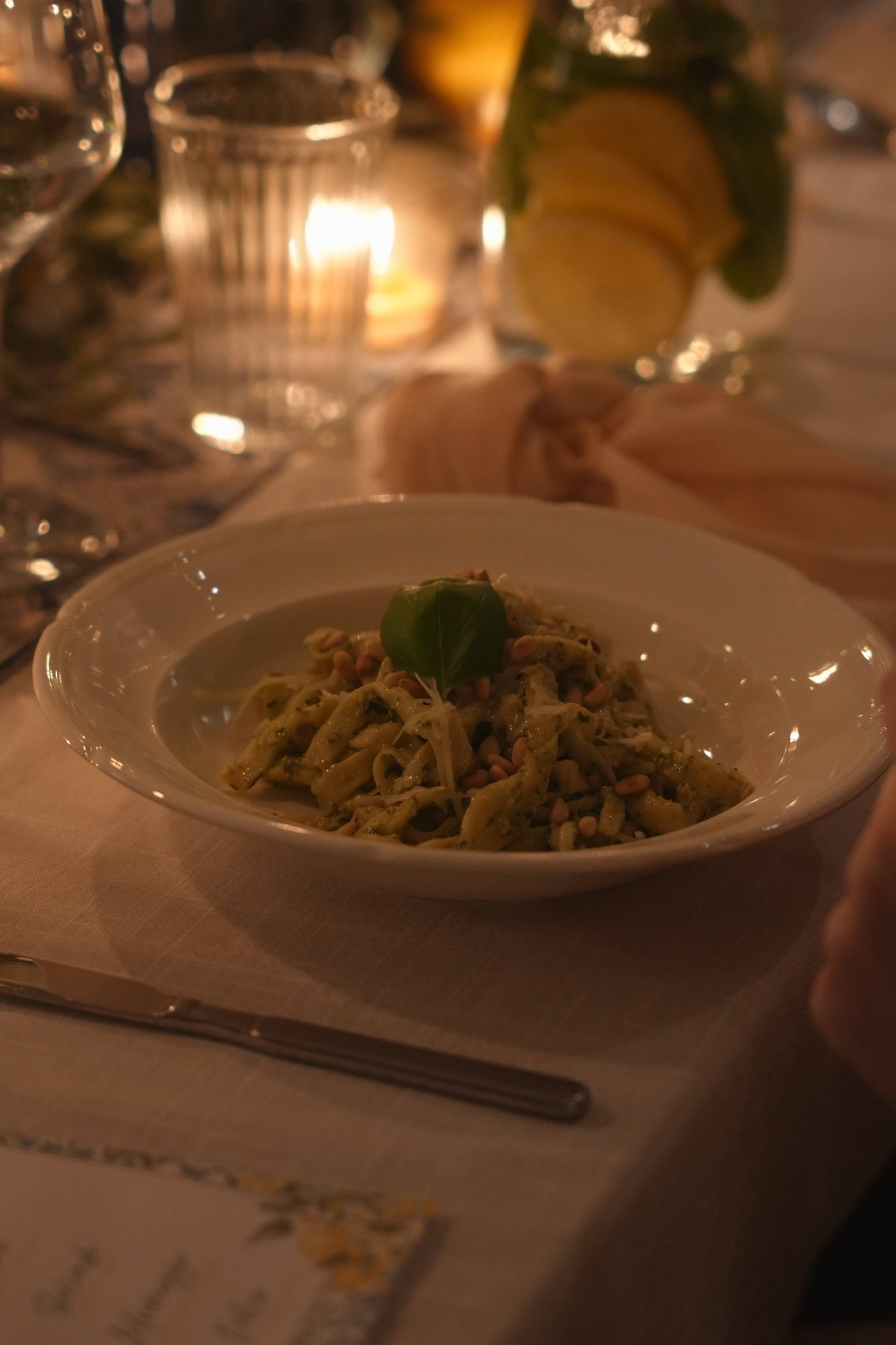 Pasta al pesto plated, candle and carafe behind