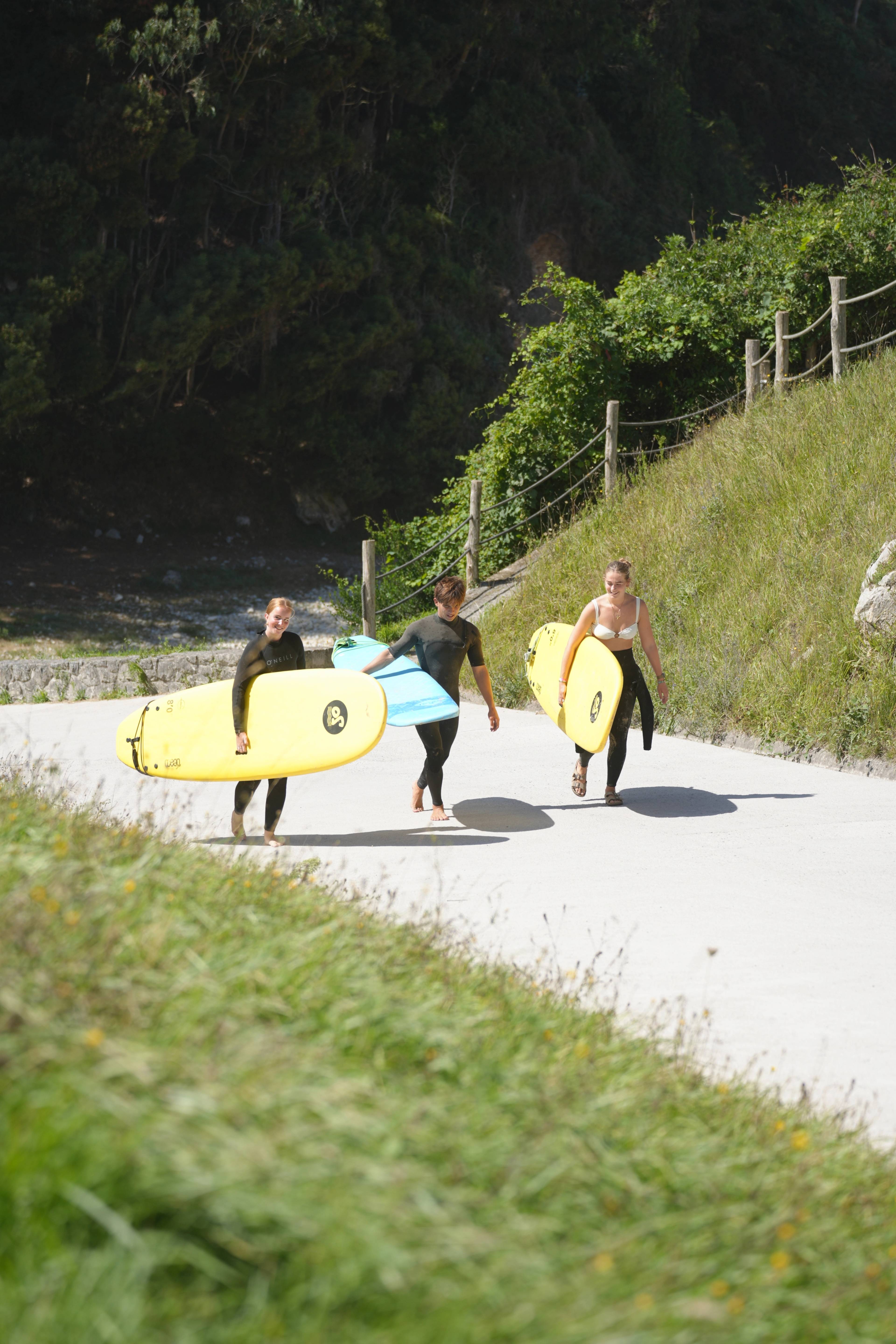 Three of us walking back up the road from the beach, boards over our hips