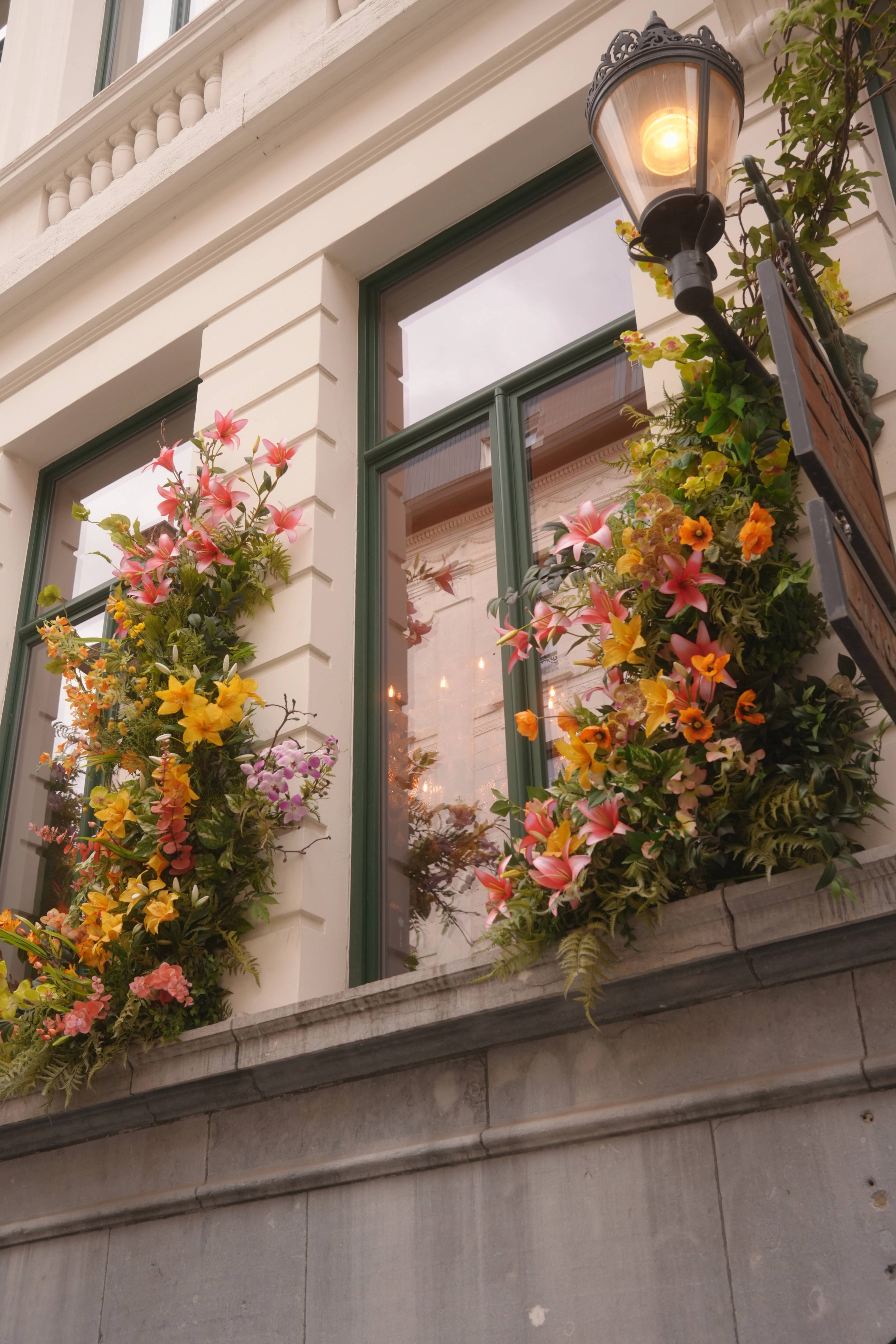 Two windows wrapped in pink and yellow flowers, a street lamp lit at midday