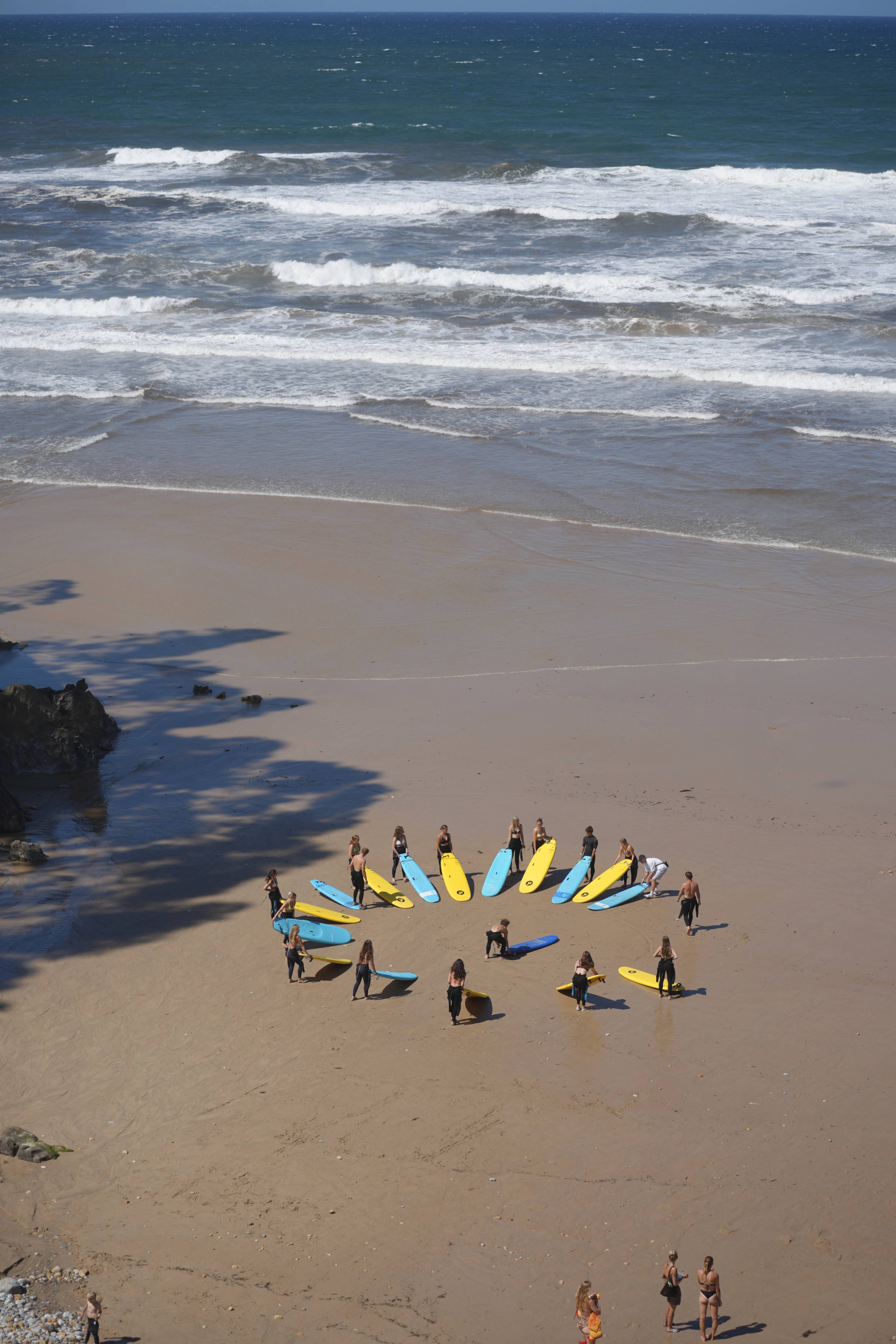 From above — the group forming a circle around their boards on the wet sand